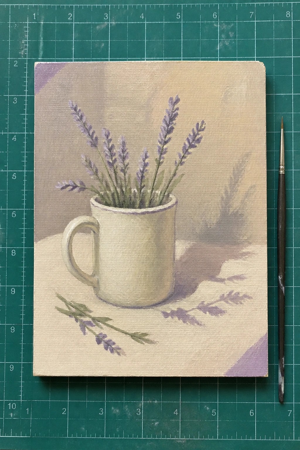 Painting of lavender sprigs in off-white mug on beige surface beside paintbrush.