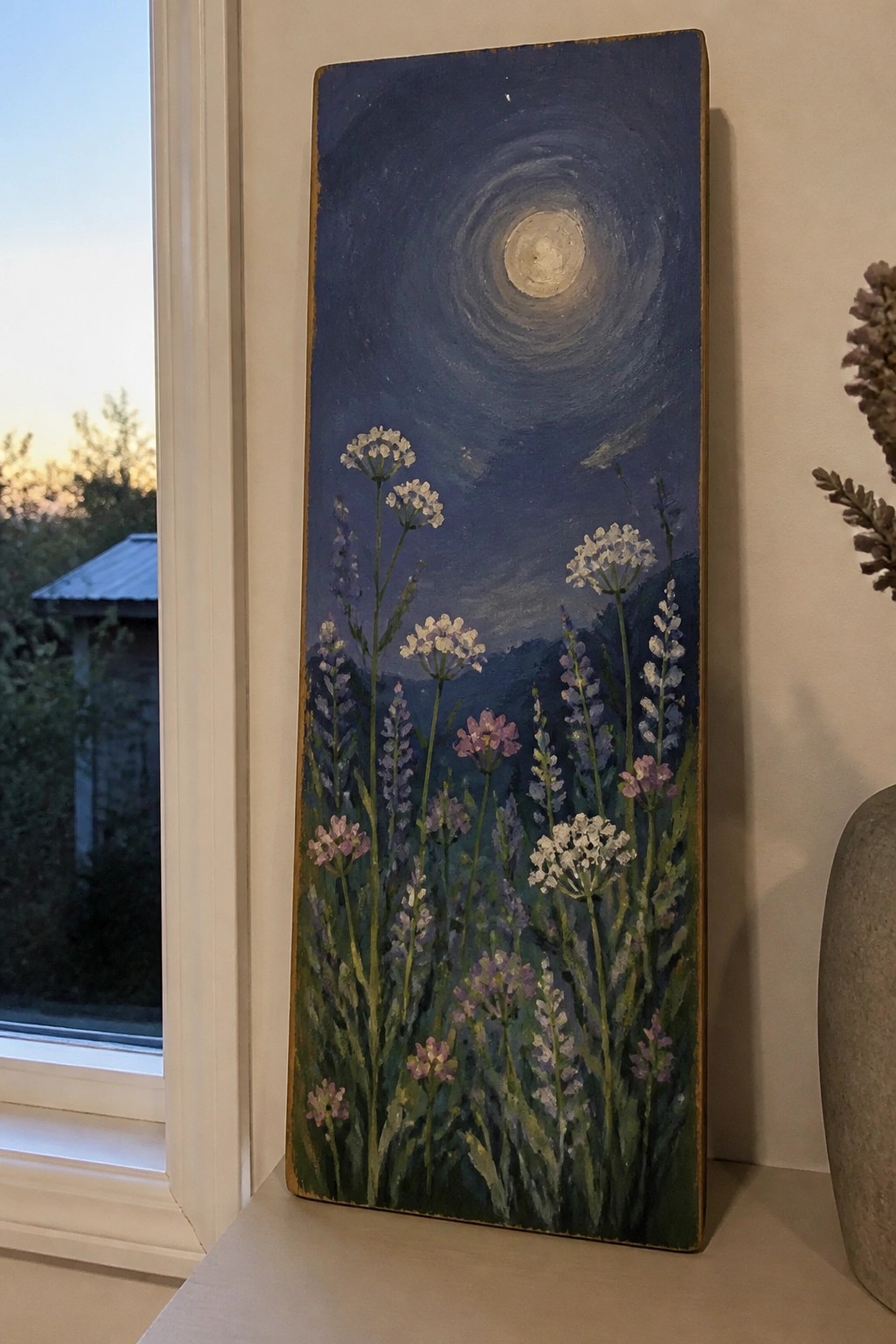 Tall painting of purple and white wildflowers beneath a glowing moon in blue sky.