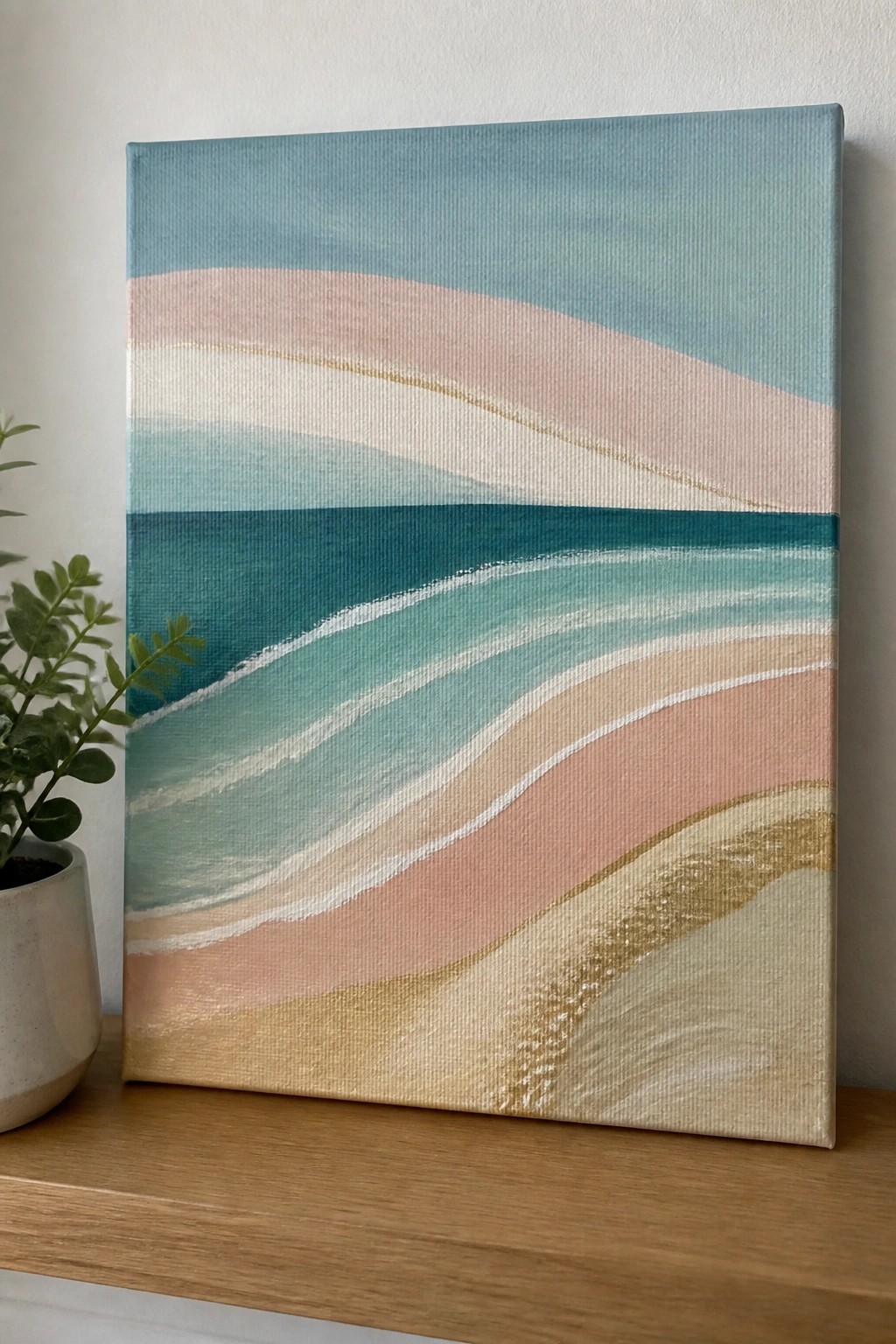 Abstract beach wave painting in blues and pinks with gold accents beside potted plant