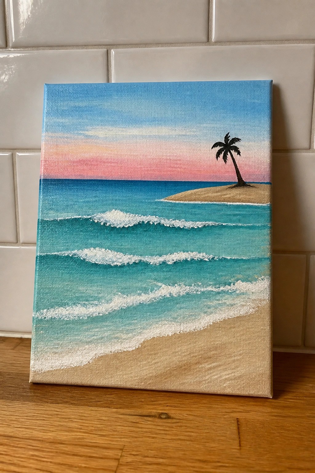 Acrylic painting of sunset over turquoise ocean waves with lone palm tree on sand.