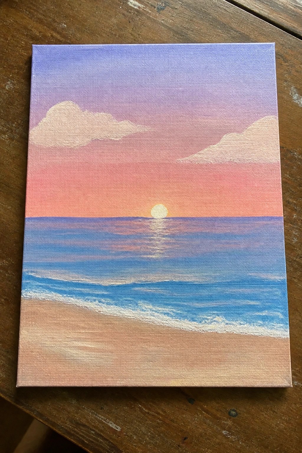 Canvas painting of beach sunset with purple-pink sky, setting sun, and blue waves.