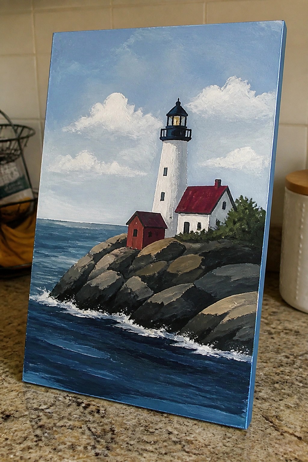 White lighthouse with black top and red-roofed buildings on rocky ocean shore