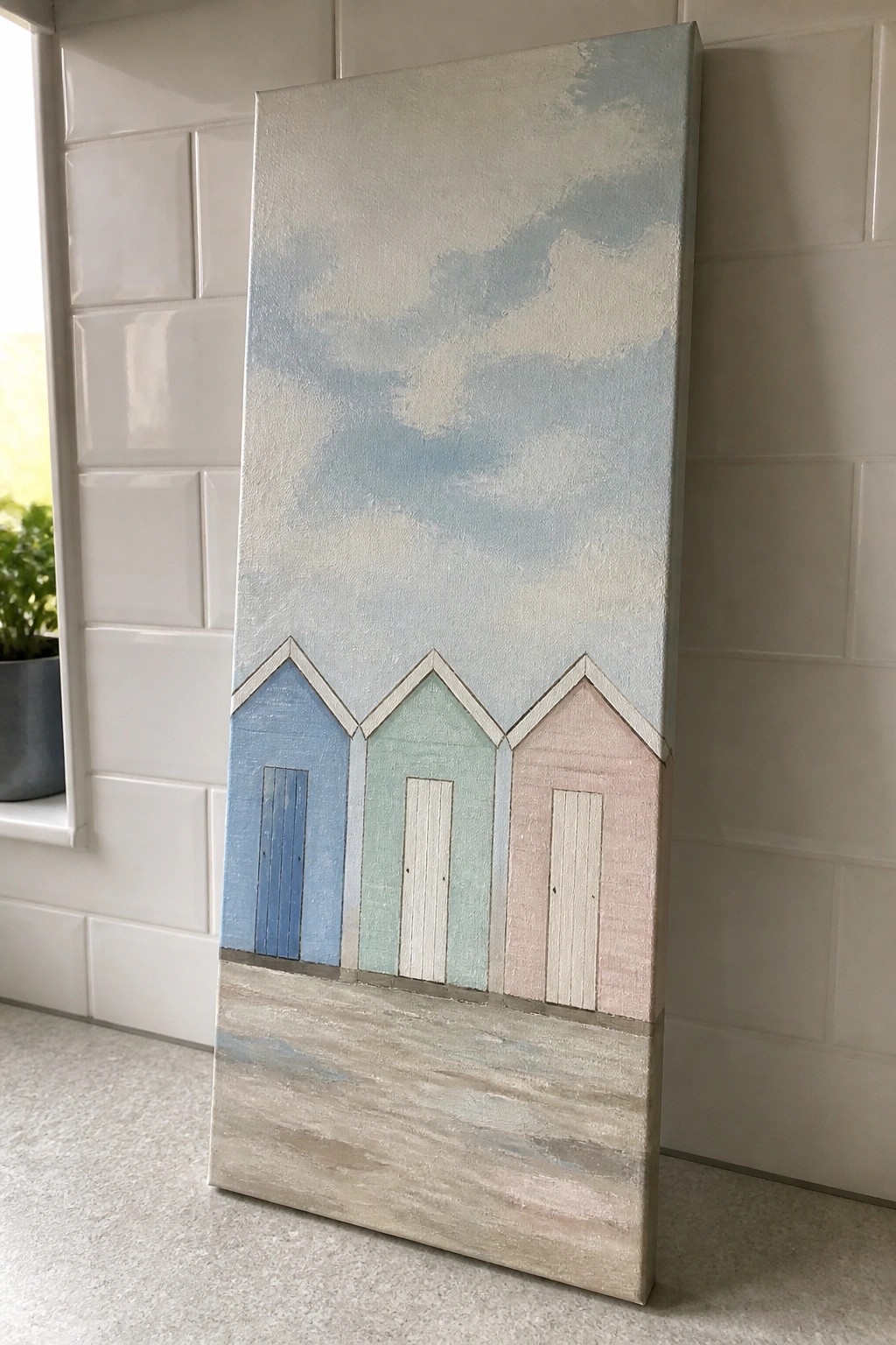 Tall canvas painting of three pastel beach huts against white tiled wall