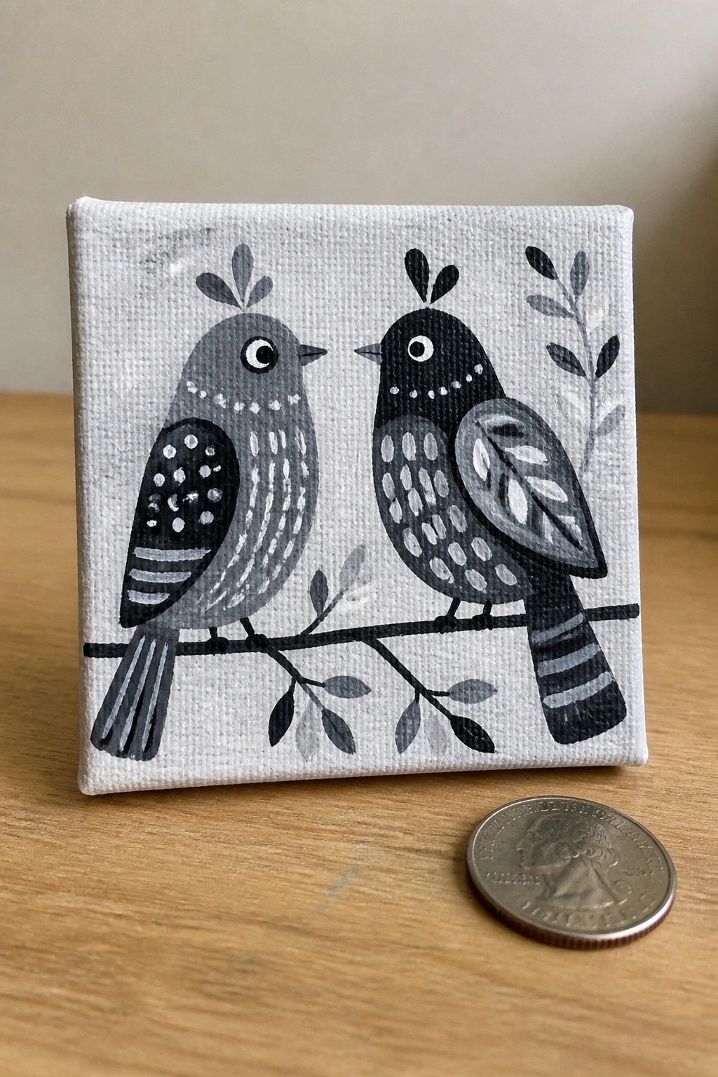 Small square canvas with two black and gray birds facing each other on a branch next to a US quarter.