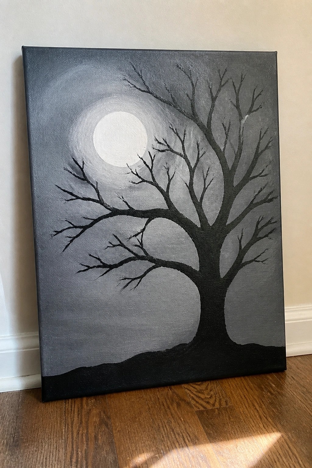Acrylic painting of a bare tree silhouette against a full moon on a dark gray background with a black ground area.