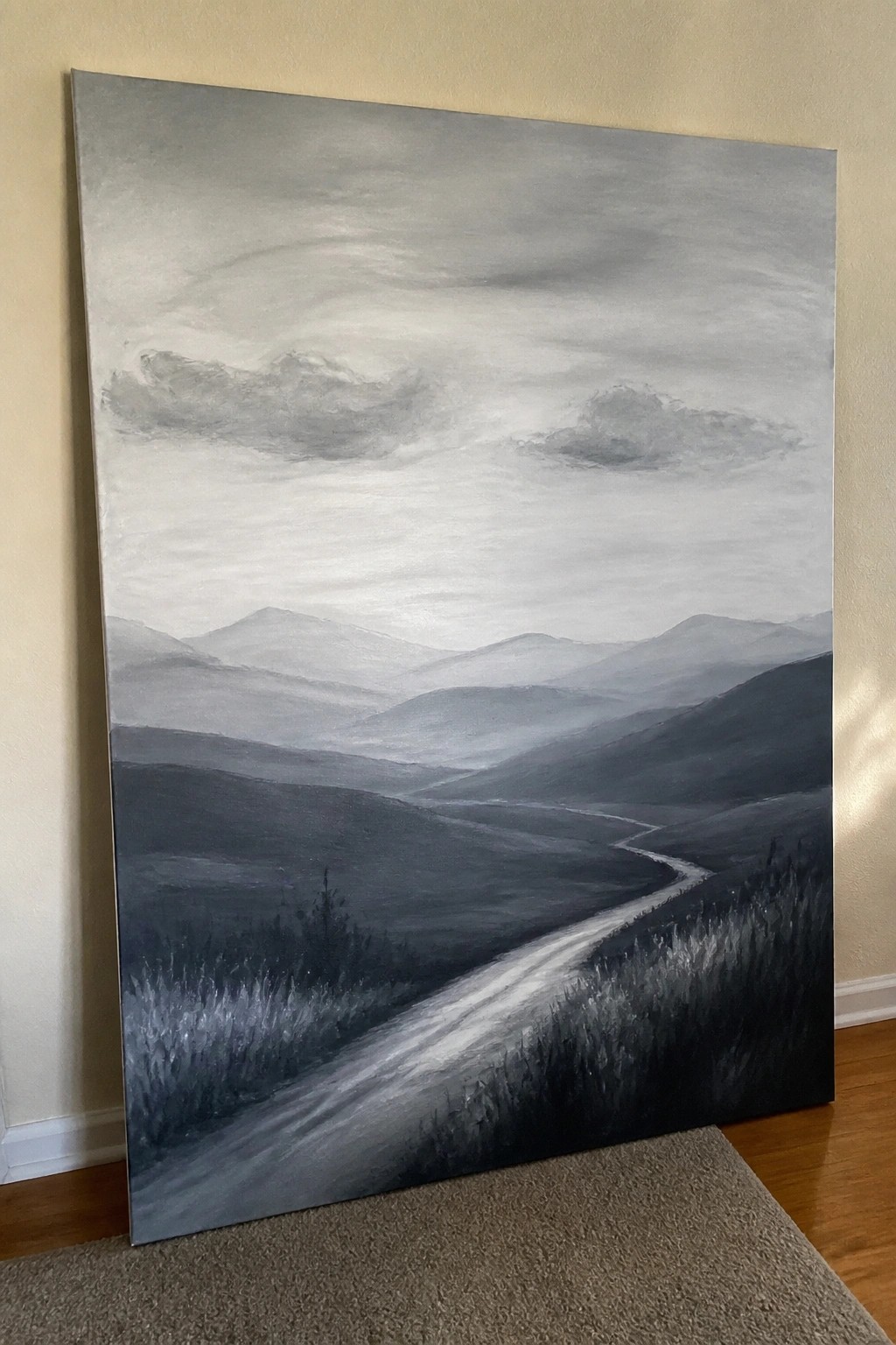Large grayscale painting of misty mountains and winding path leaning against wall.