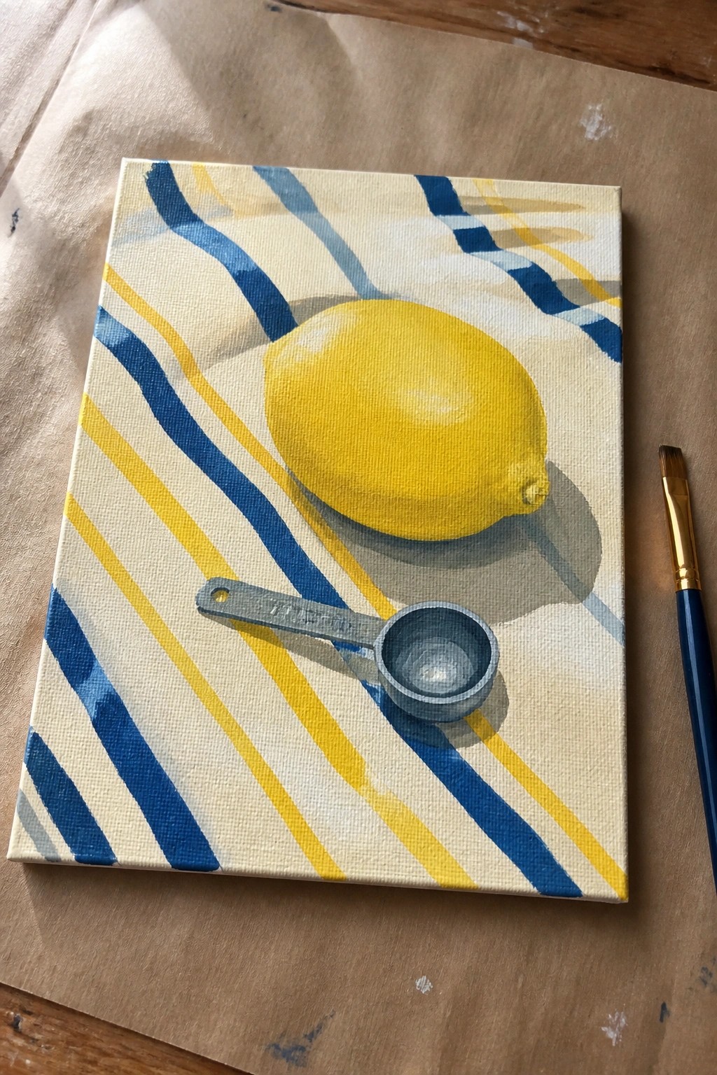 Yellow lemon and measuring spoon on blue-yellow striped canvas with paintbrush nearby