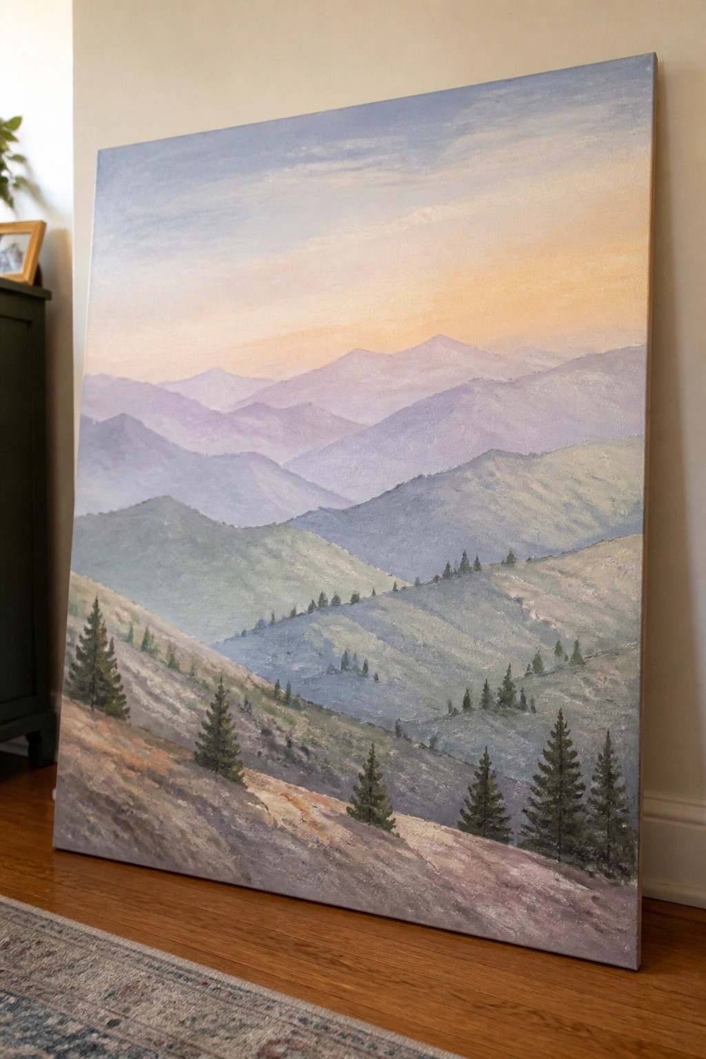 Large painting of layered mountains with pine trees under orange-pink sky indoors