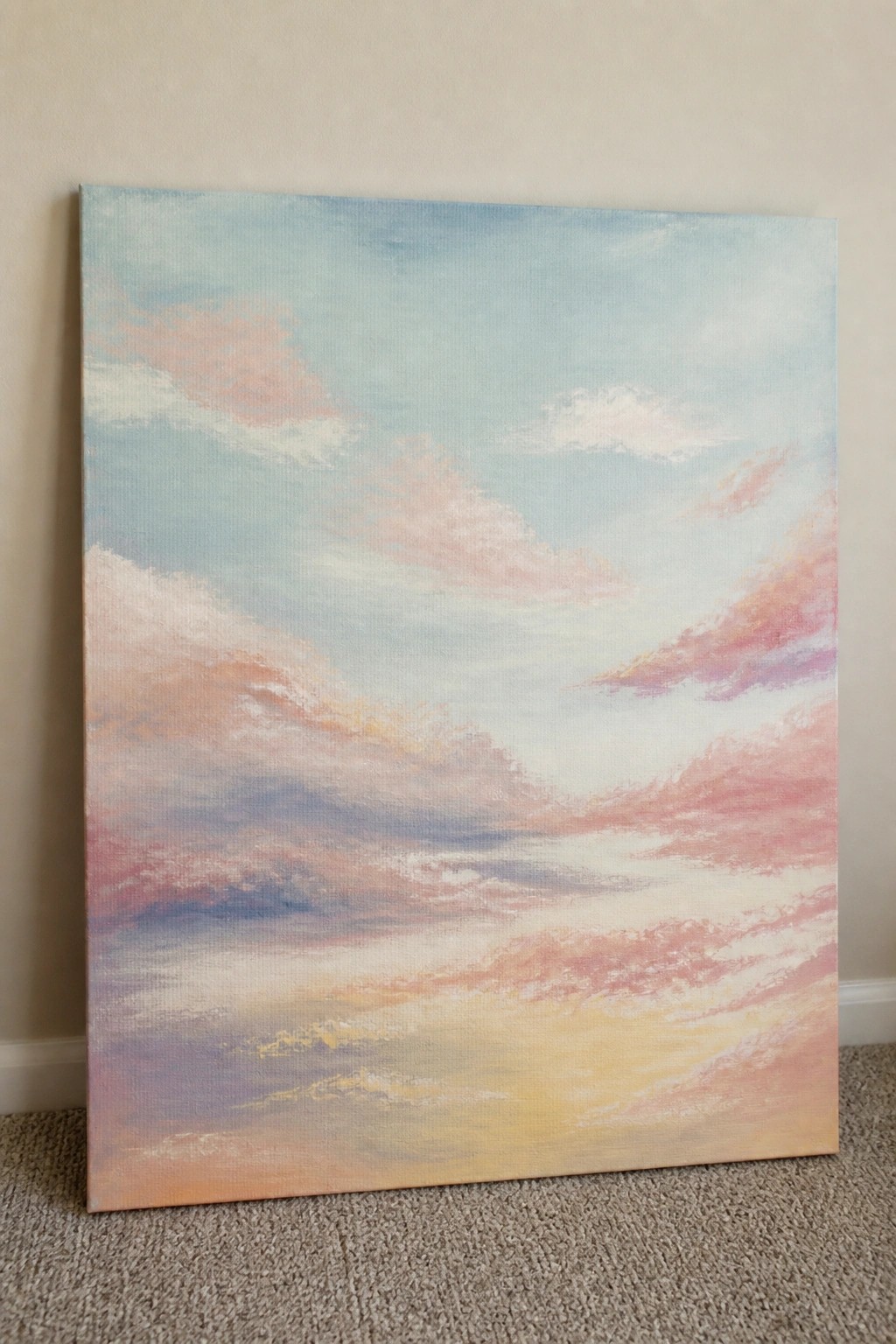 Pastel sky painting with pink and orange clouds leaning against wall on carpet