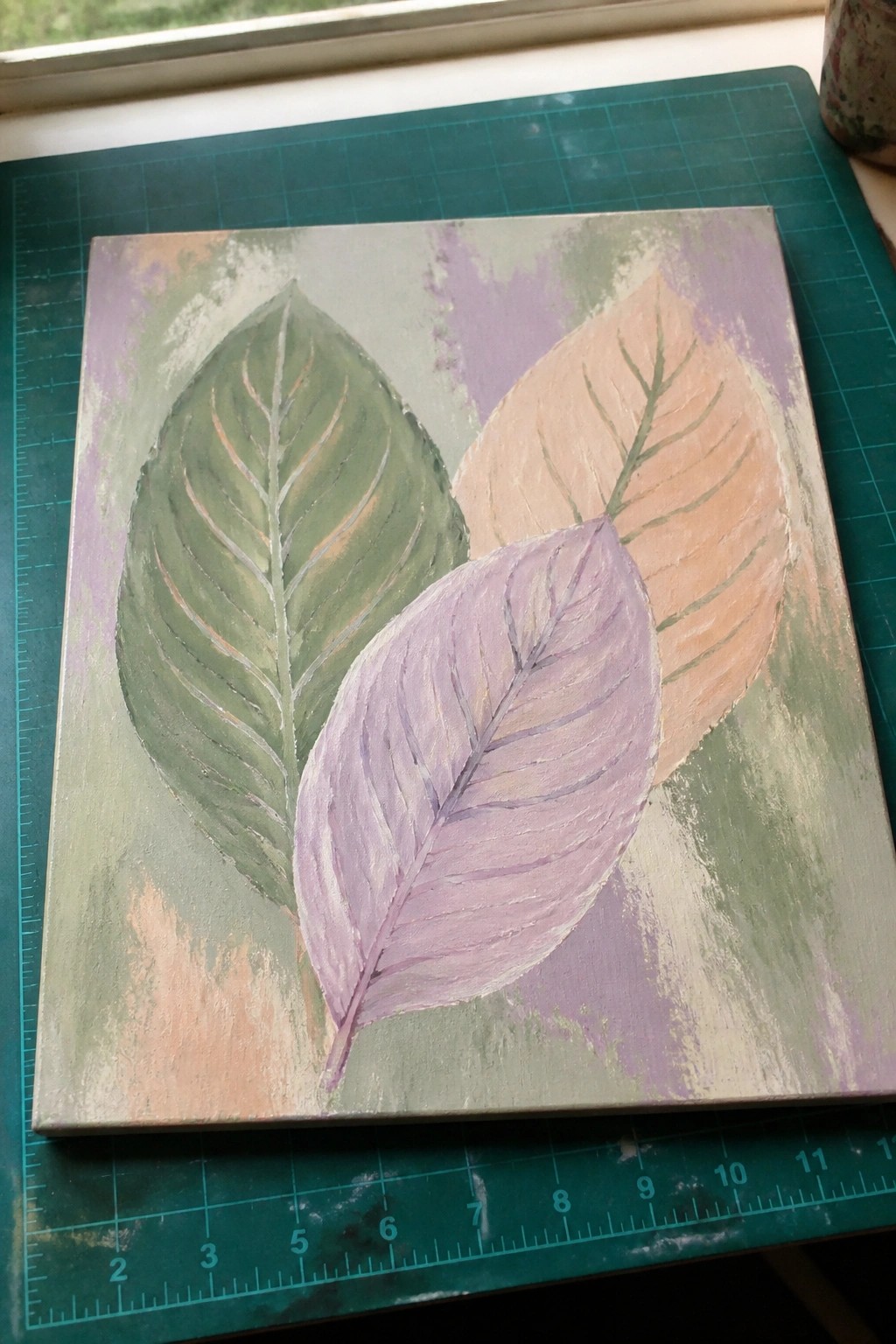Three overlapping leaves painted green, purple, and peach on abstract canvas.