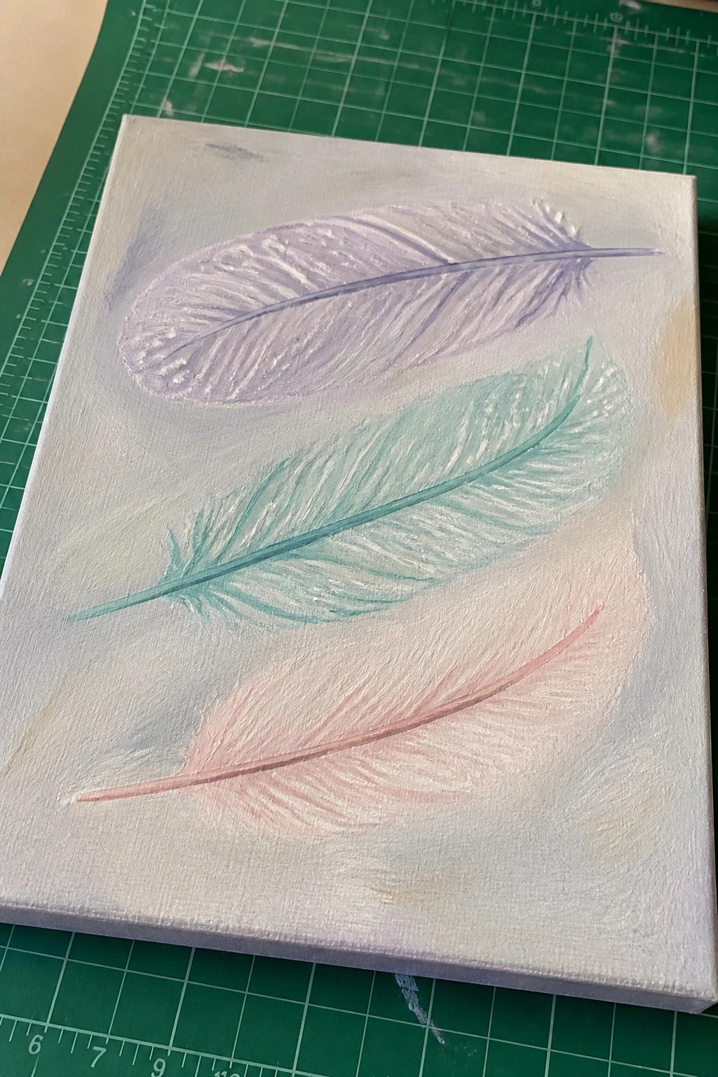 Canvas with three pastel feathers in lavender, mint green, and pink.