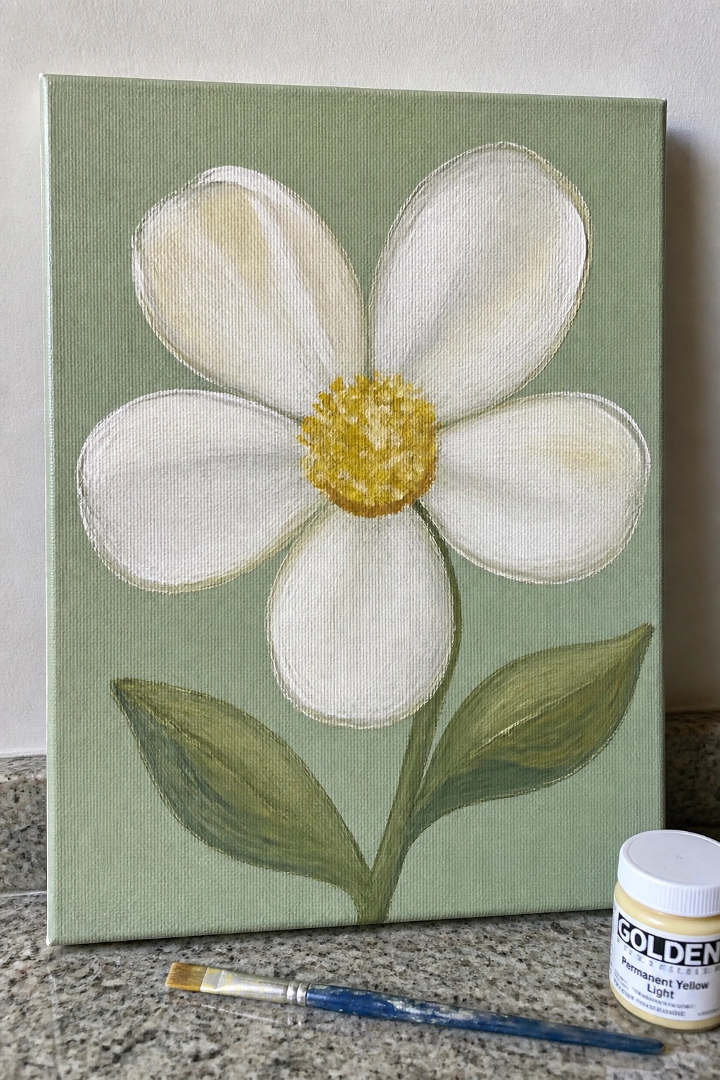 Acrylic painting of white flower with yellow center, green leaves, paintbrush, and jar.