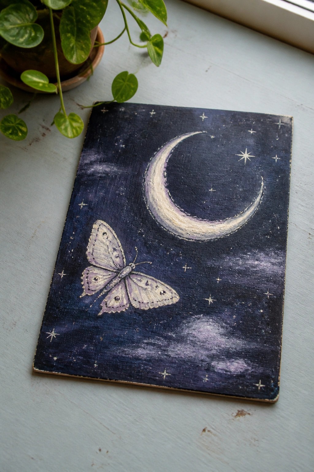 Purple butterfly beneath crescent moon and stars on dark blue painted night sky