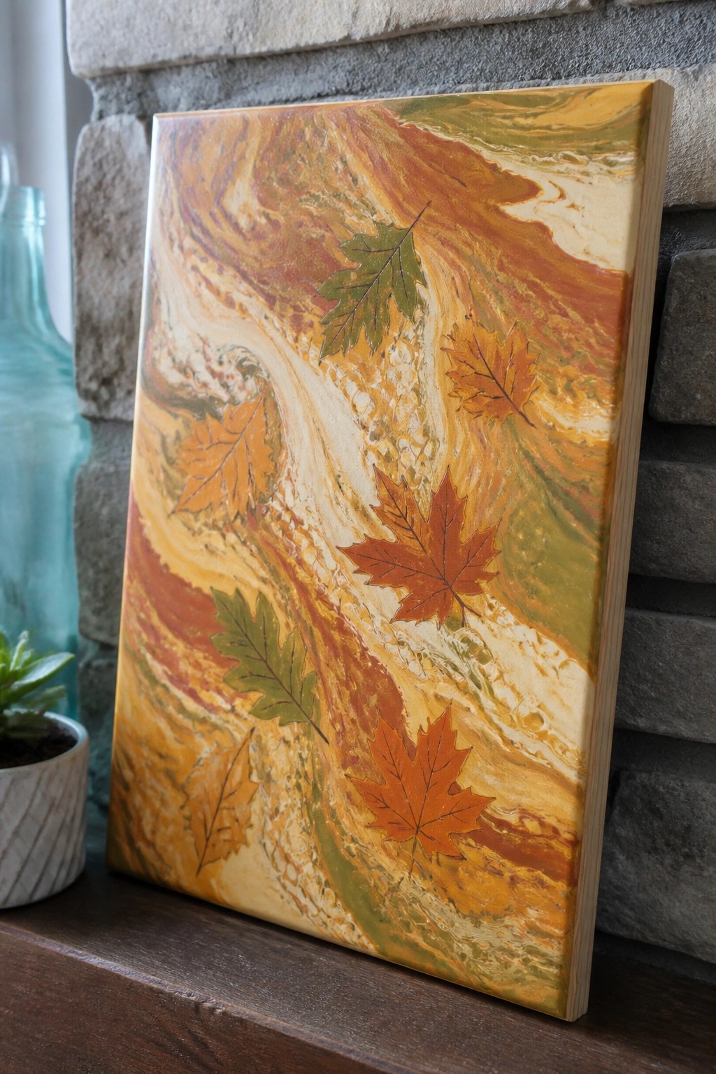 Marbled autumn canvas with orange leaves against stone wall and blue bottle