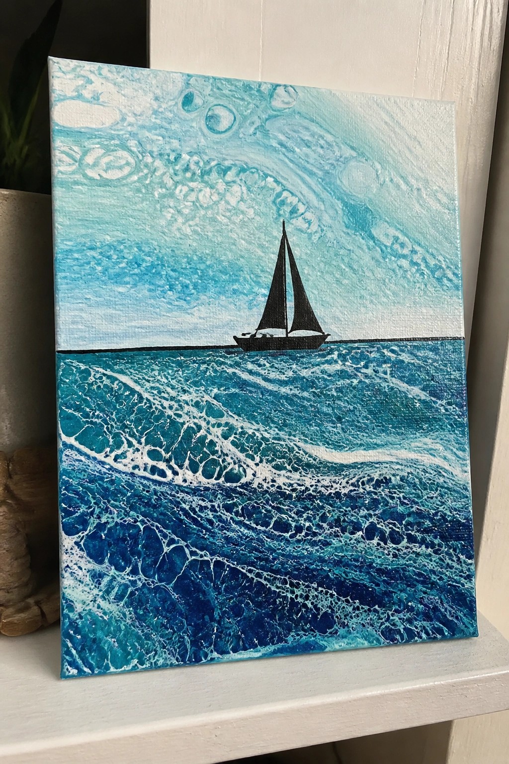 Black sailboat silhouette on marbled blue waves beneath abstract turquoise sky in fluid art painting
