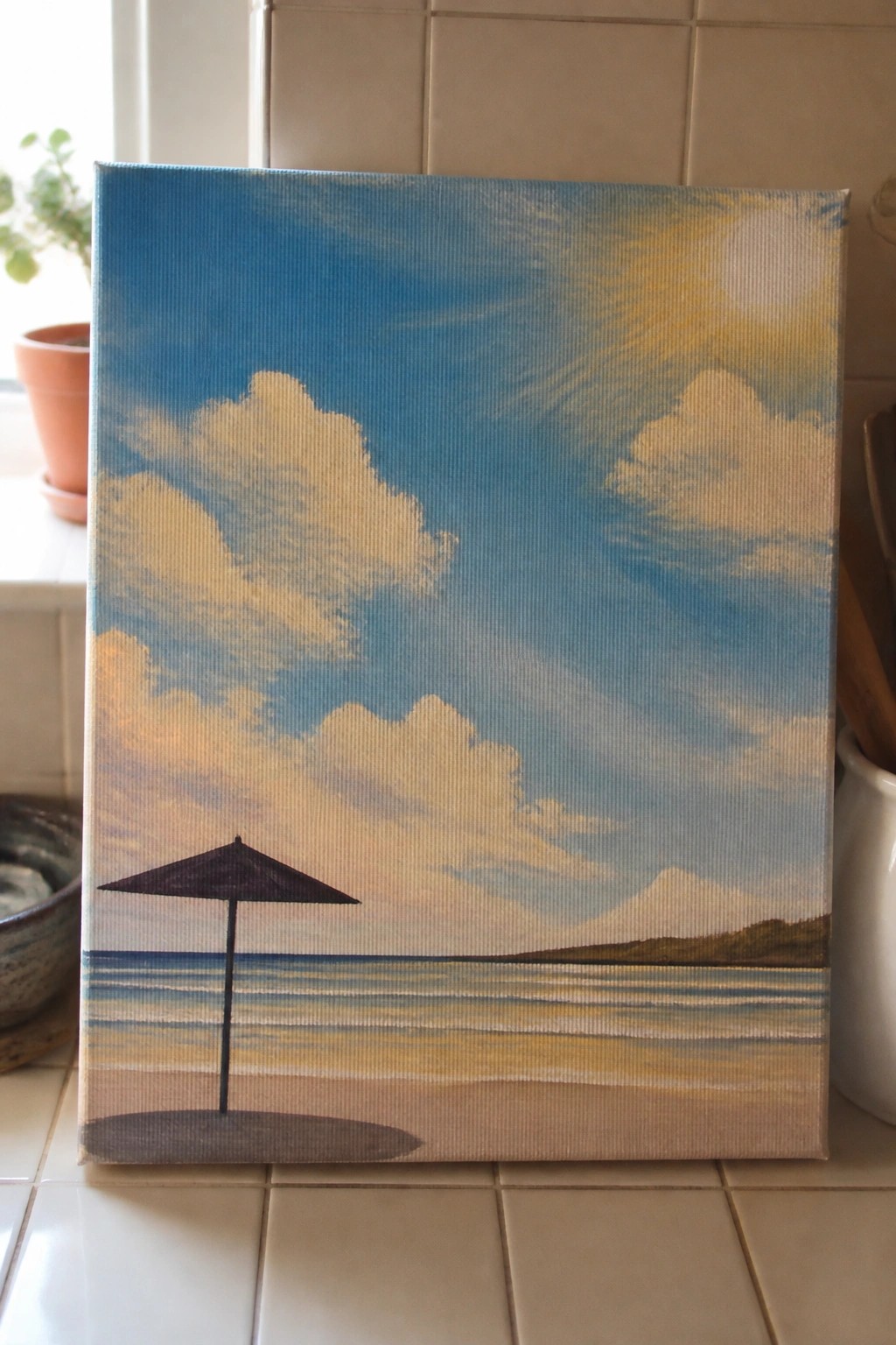 Painting of sunny beach with black umbrella on sand, striped ocean, and cloudy sky.