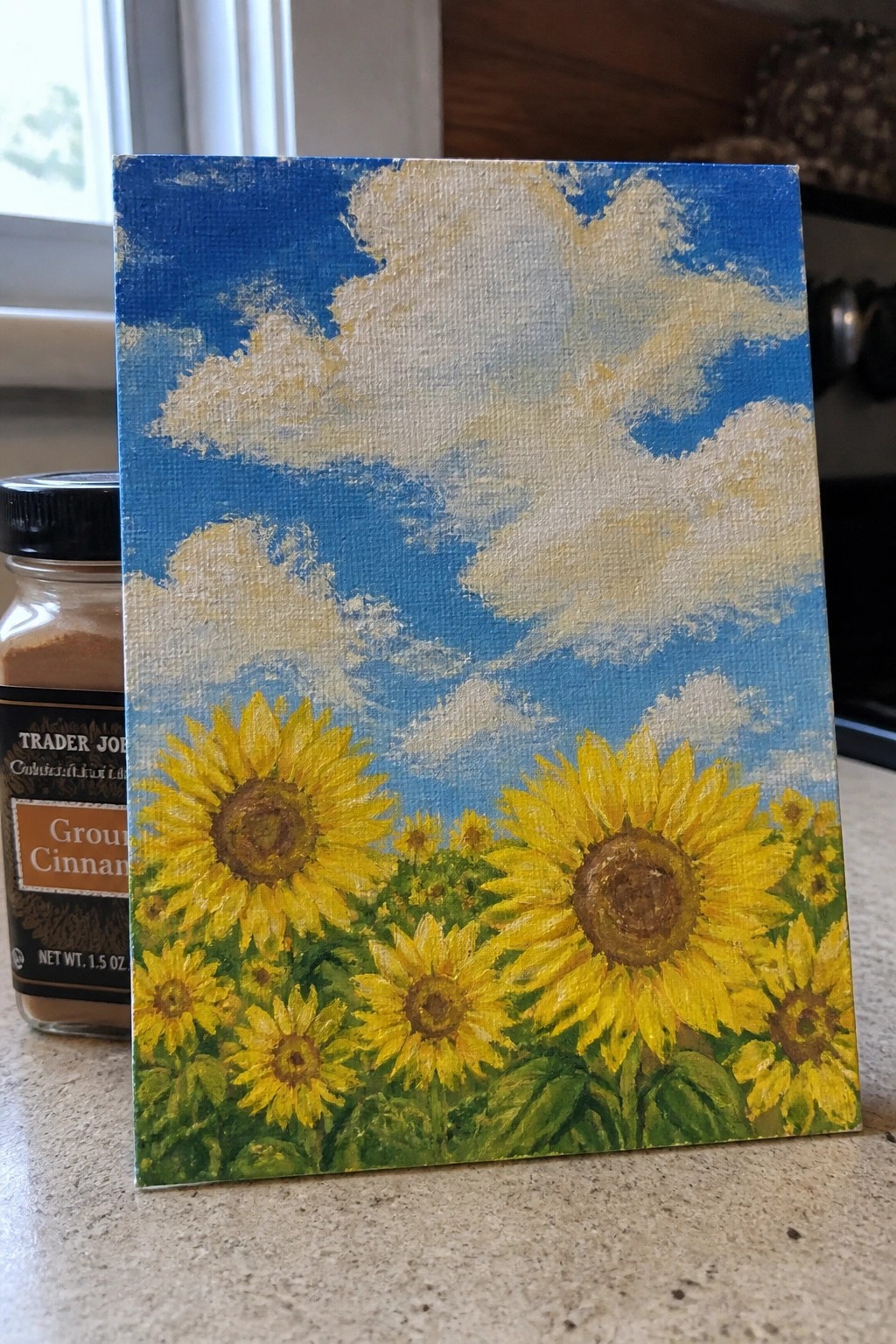 Yellow sunflowers painting beside Trader Joe's cinnamon jar on speckled countertop