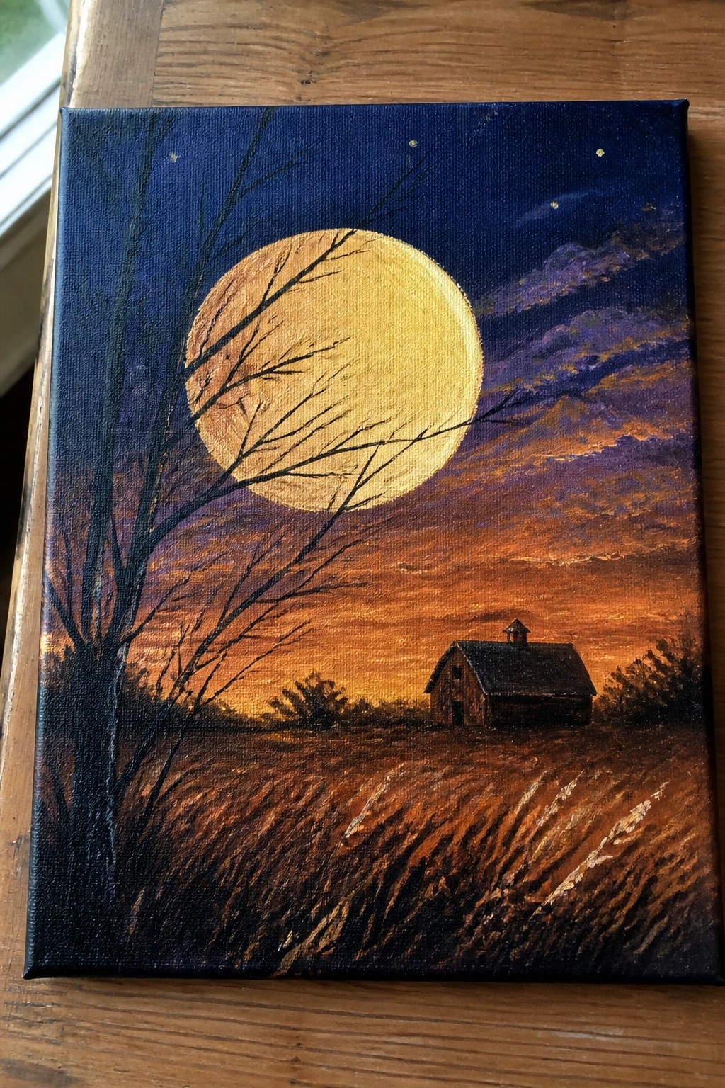 Acrylic painting of a large yellow moon in a dark blue sky above a barn in a field with a silhouetted tree on the left.