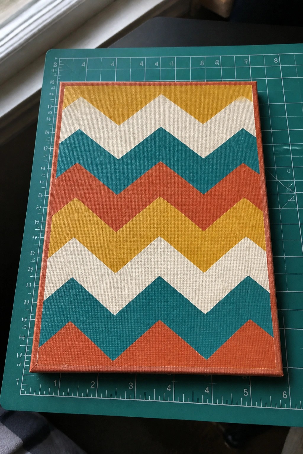 Colorful chevron-patterned canvas in yellow, teal, orange and white on green cutting mat