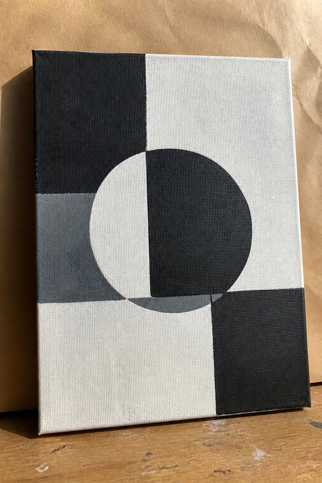 Abstract canvas painting of black-and-white circle amid gray and rectangular blocks.