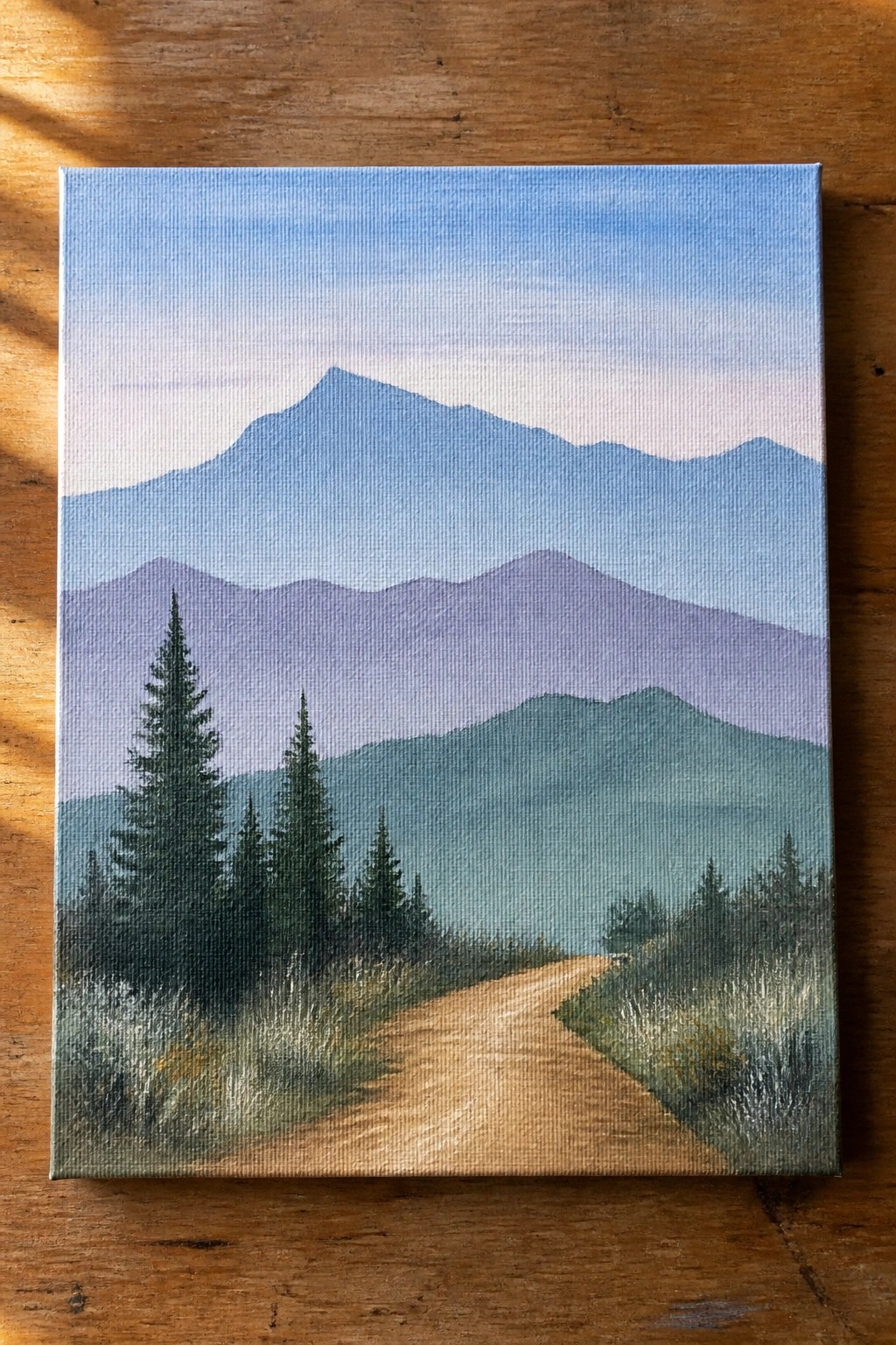 Winding dirt path through pine trees toward layered blue and purple mountains on canvas.