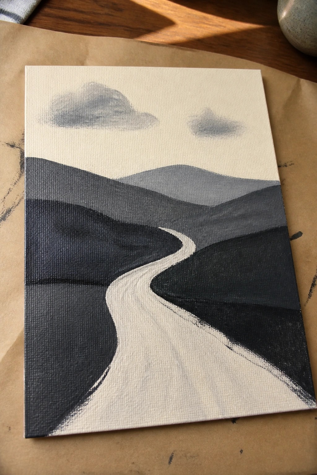 Abstract painting on canvas showing winding white path through layered gray hills and clouds