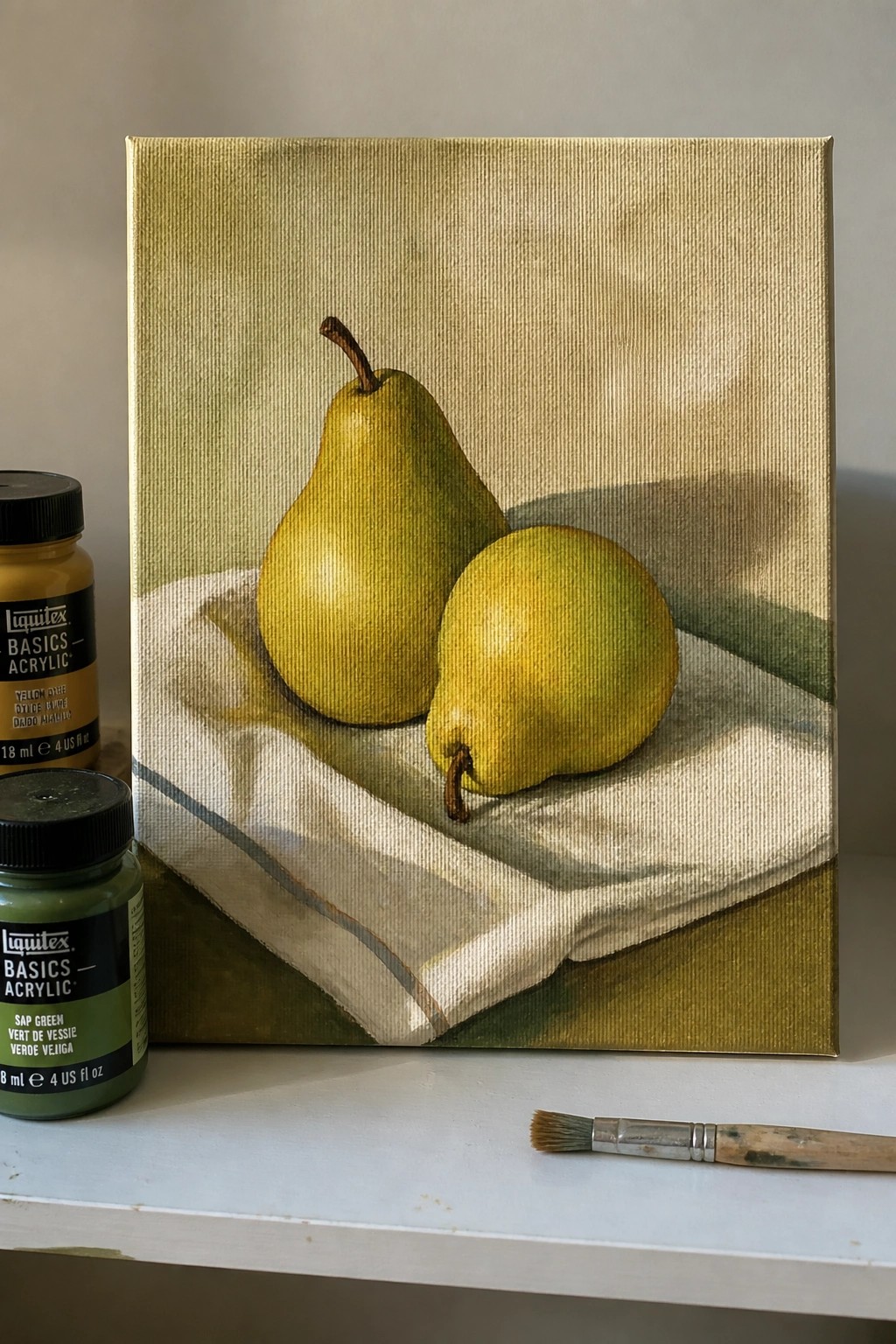 Still life acrylic painting of two pears on white cloth with paint jars and brush