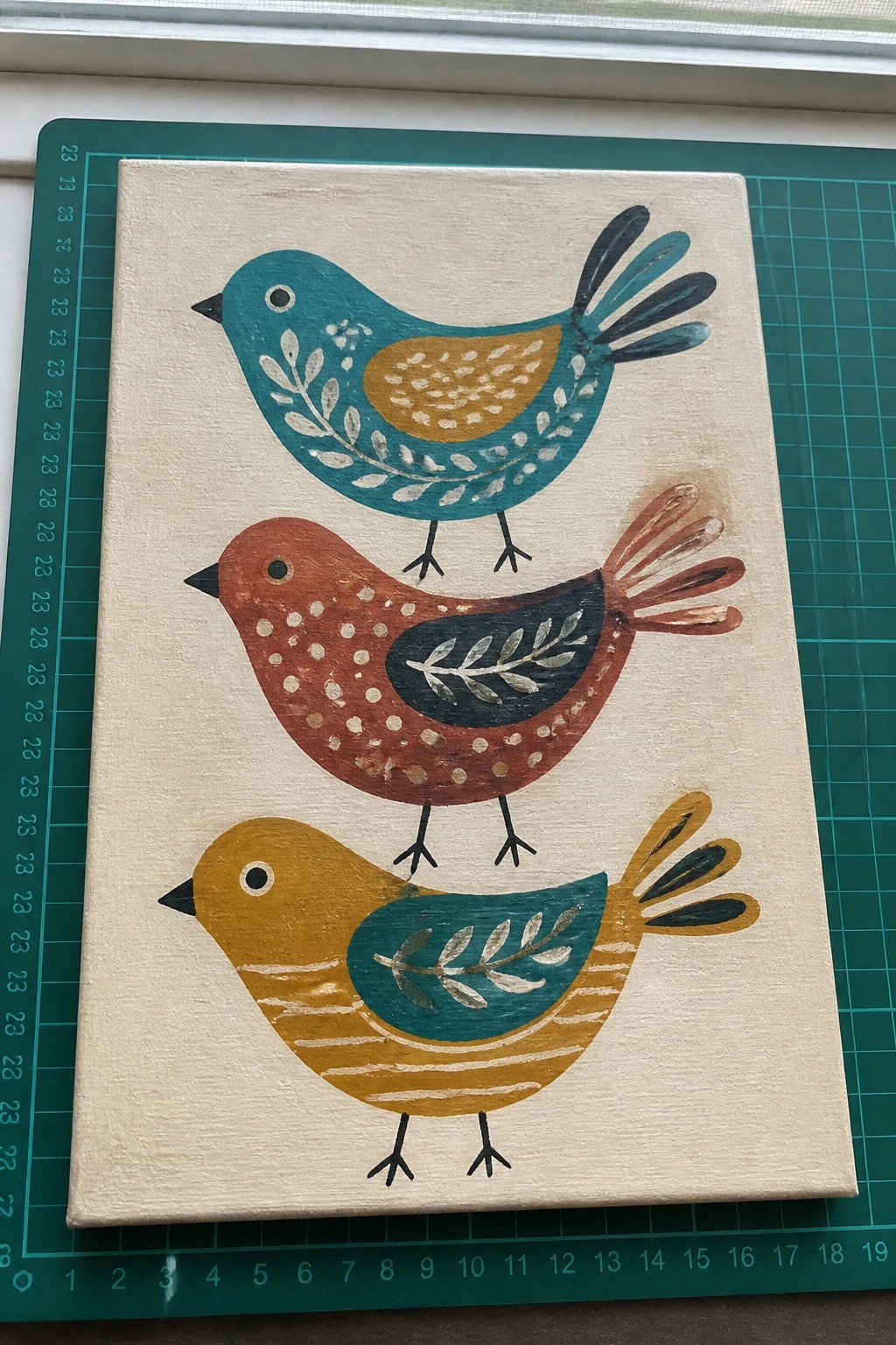 Three colorful folk-art birds stacked on beige canvas painting