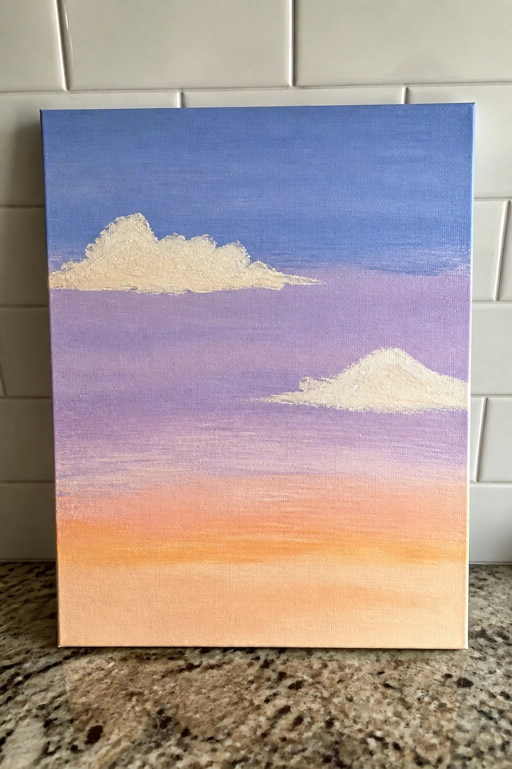 Canvas painting of blue-purple-orange gradient sky with two white clouds on counter.