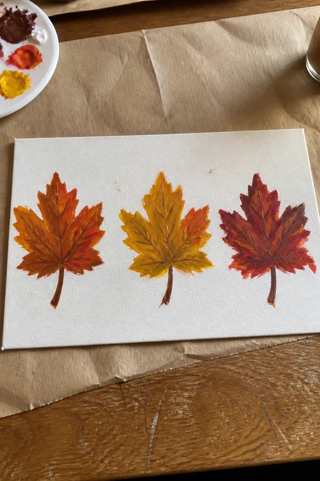 Three autumn maple leaves in yellow, orange, and red painted on white canvas.