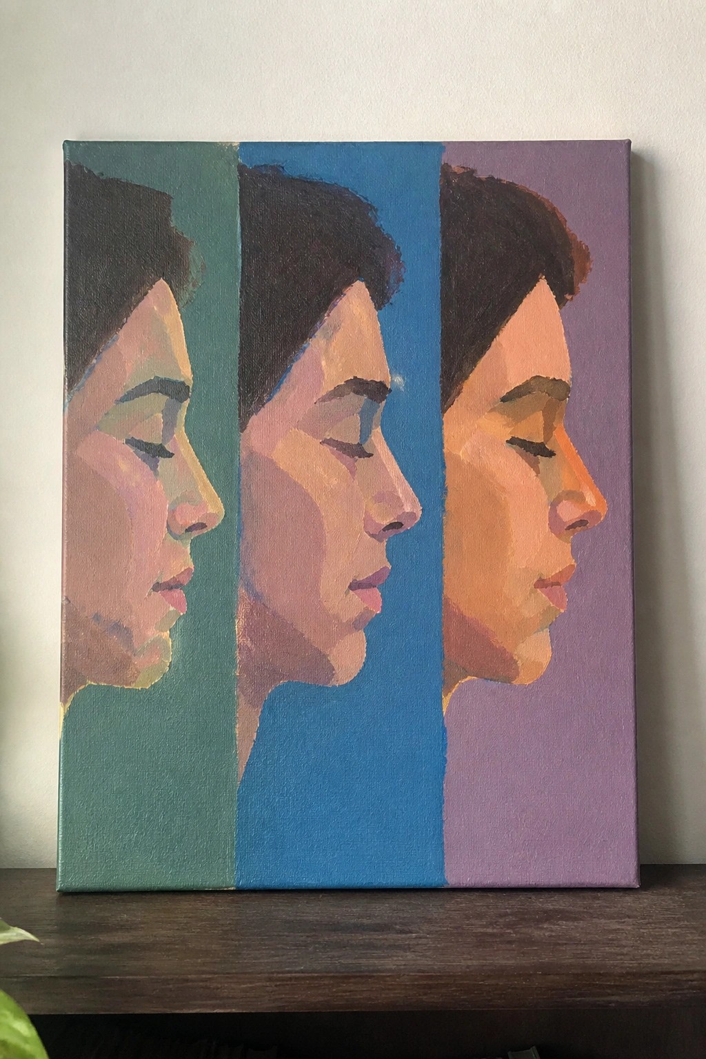 Three profile portraits of a woman painted on teal, blue, and purple canvas panels.