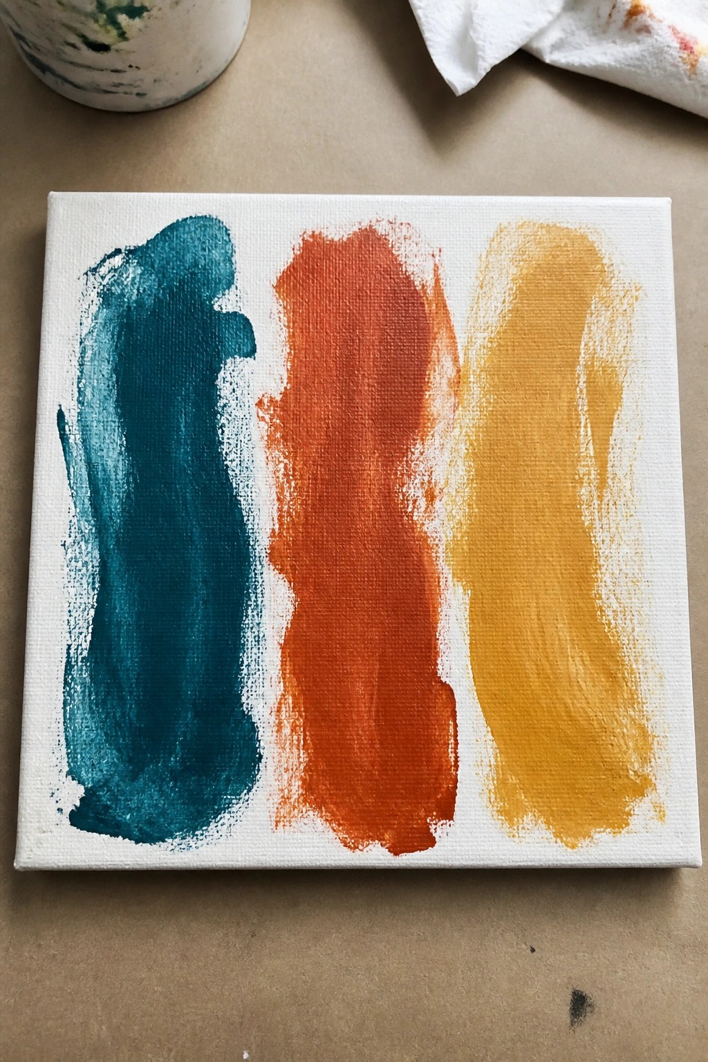Small white canvas with thick vertical strokes of teal, orange, and yellow paint.