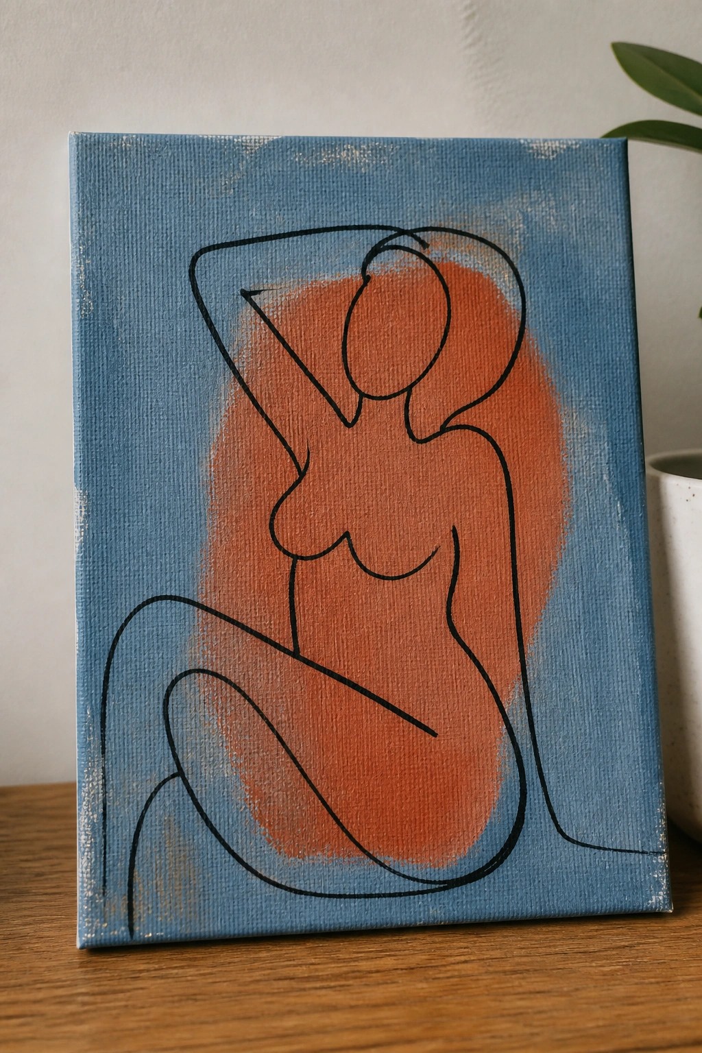 Continuous black line art of nude woman on blue-orange canvas on wood table