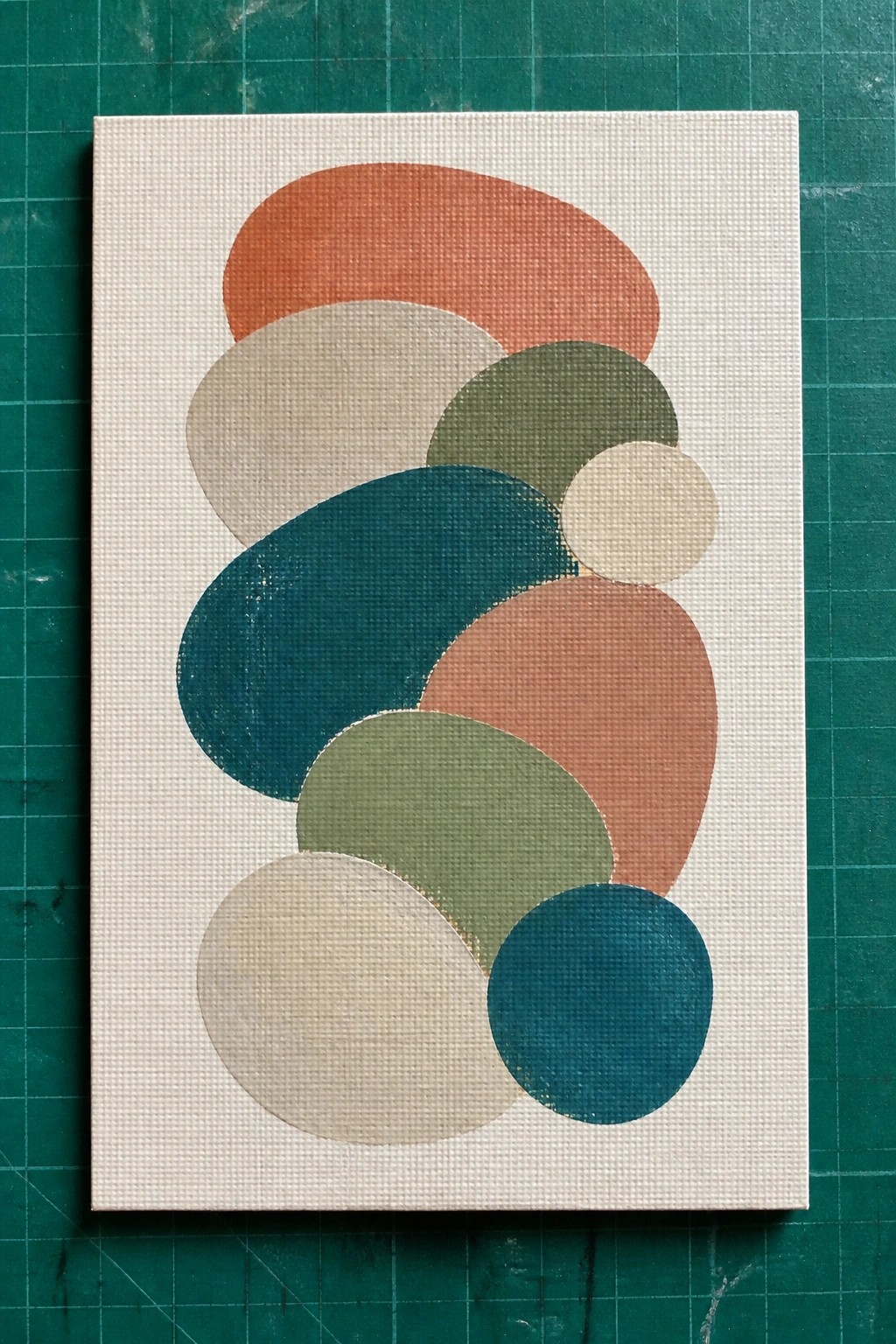 Abstract canvas with overlapping curved shapes in teal, orange, green, and beige on green mat.