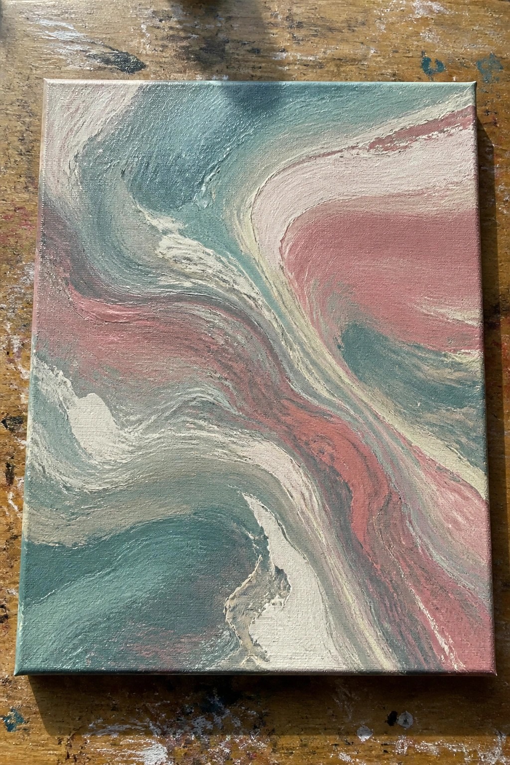 Abstract painting with swirling teal, pink, and white colors on wooden table