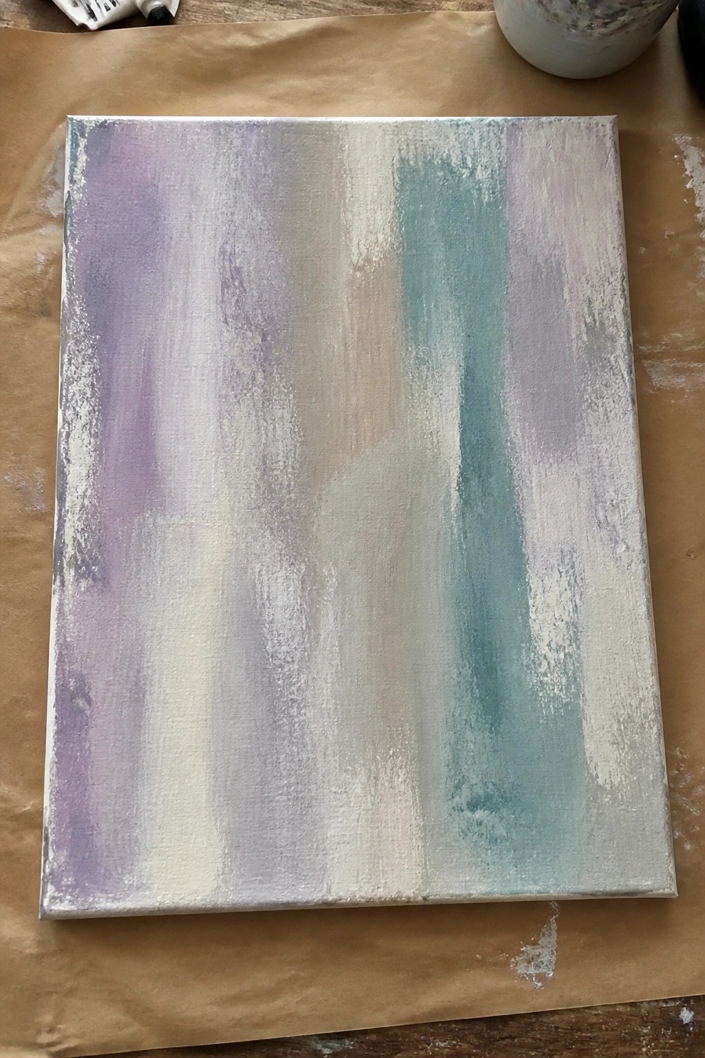 Abstract canvas with vertical pastel streaks in purple, teal, beige atop brown paper.