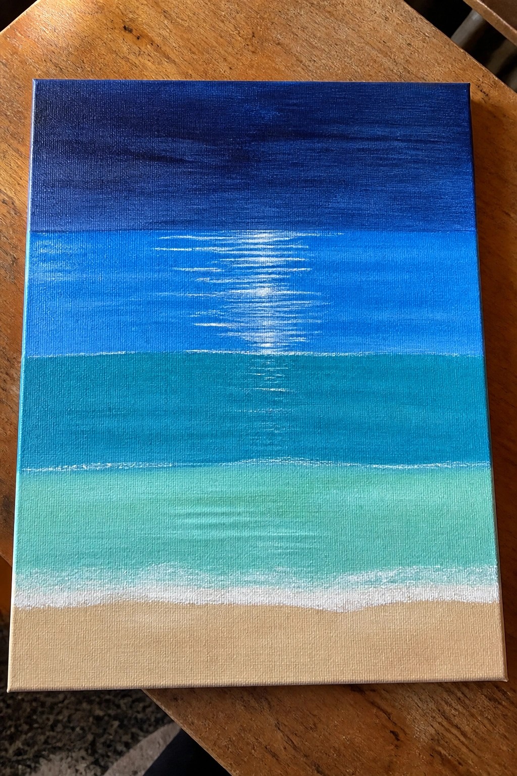 Blue gradient seascape painting with white sun reflection, teal waves, and sandy beach on wood.