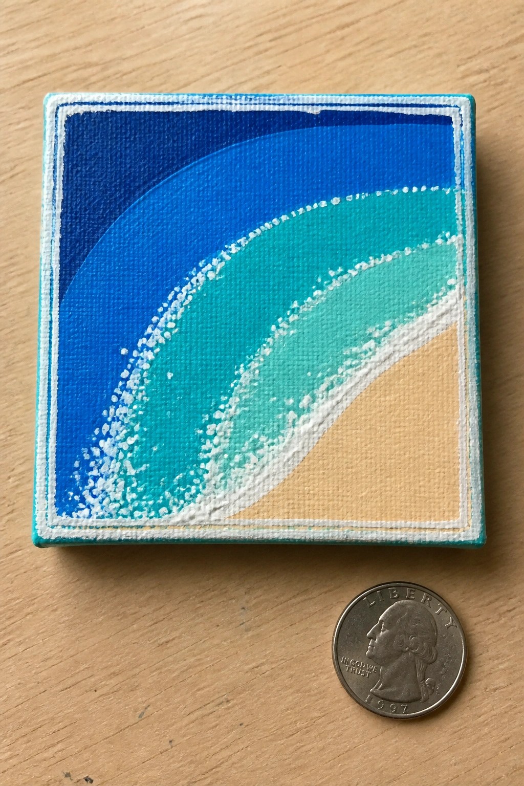 Small abstract canvas with blue-green waves beside a 1997 quarter coin