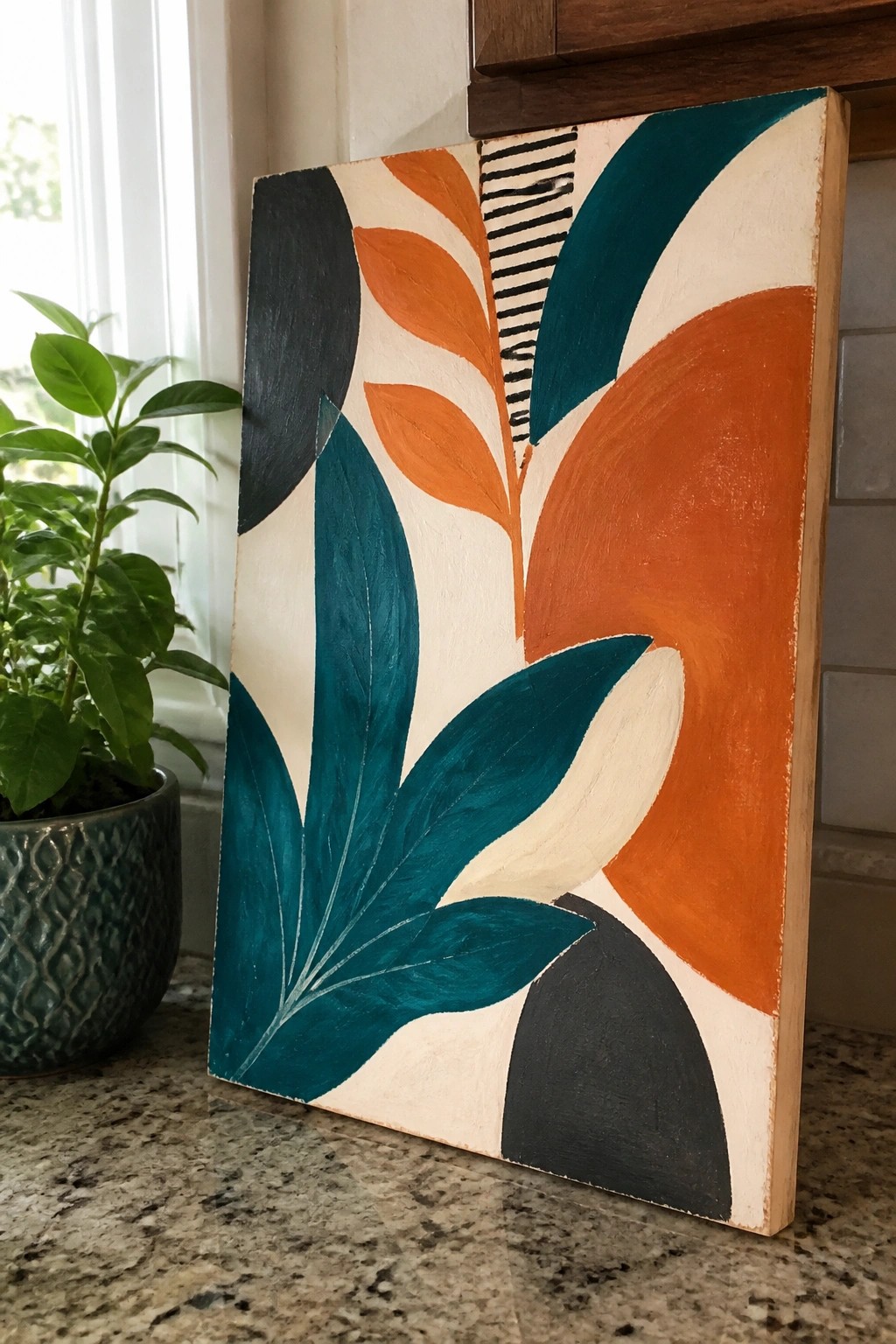 Abstract painting with teal leaves, orange curves, and black shapes on kitchen counter