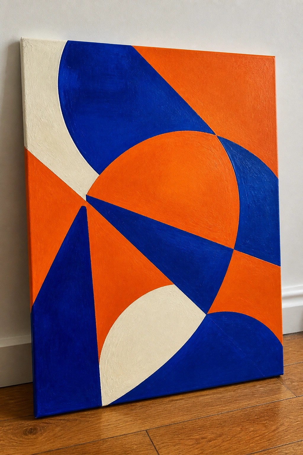 Abstract painting with blue, orange, and white curved shapes on canvas against wall on wood floor
