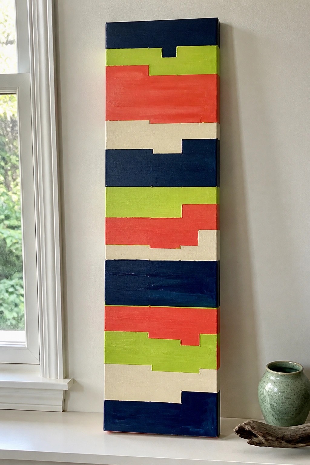 Colorful abstract painting with jagged horizontal stripes in blue, green, red, and white beside window