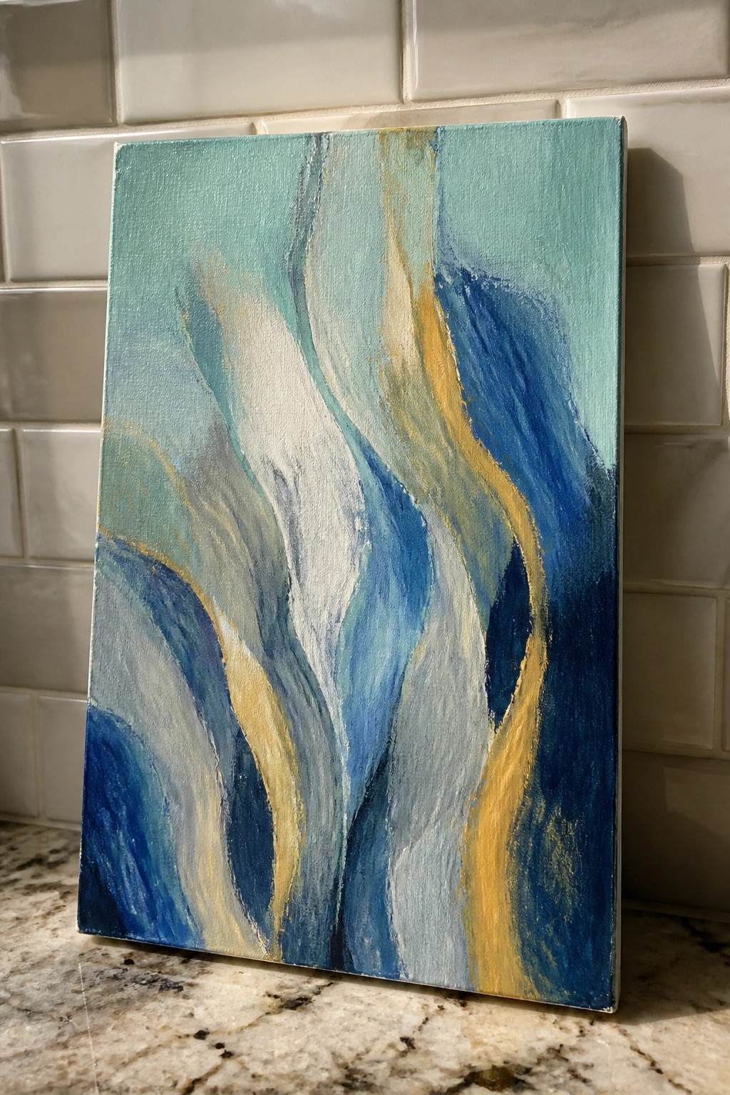 Abstract painting with swirling blues, teals, whites, and golds on canvas against tiled wall.