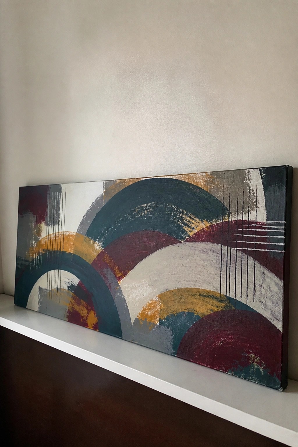 Abstract painting with overlapping arcs in teal, maroon, yellow, white, and gray on canvas.