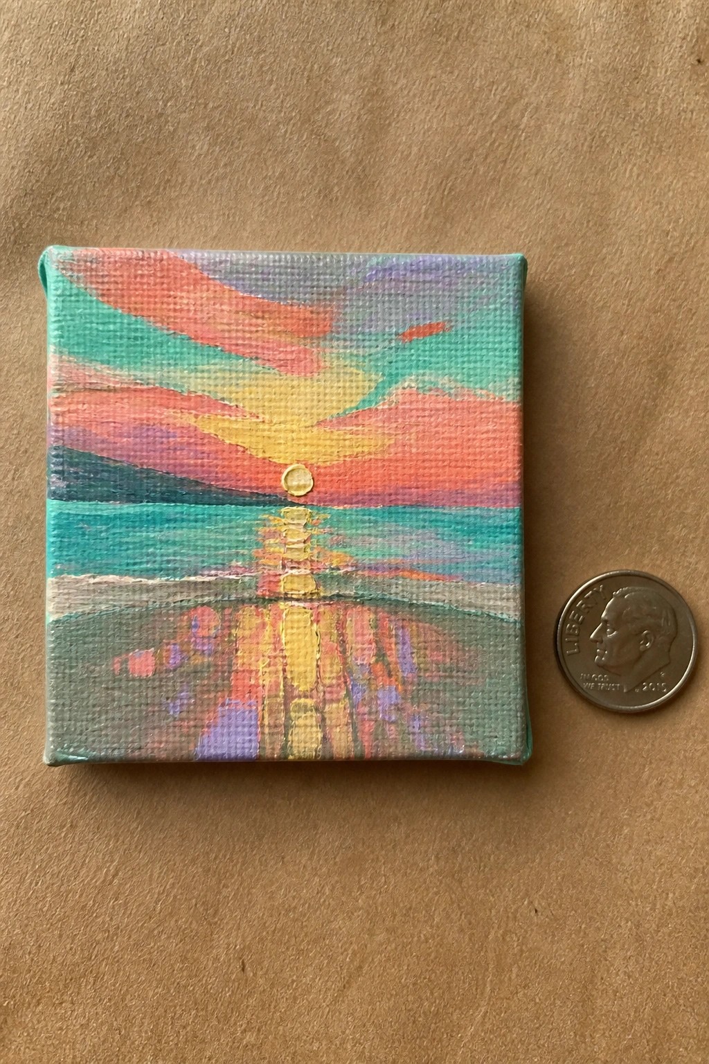 Small vibrant canvas sunset painting beside US dime for scale