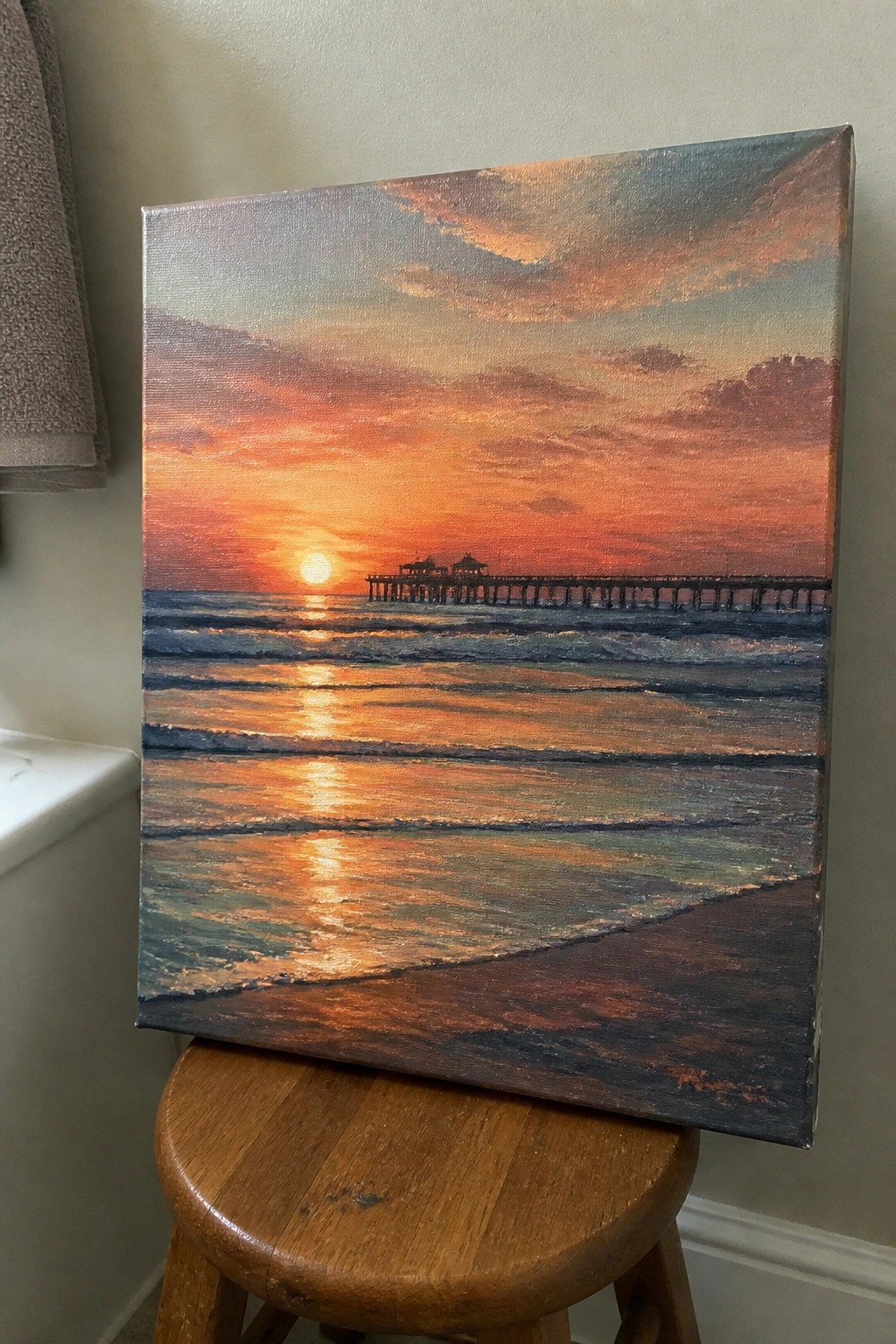 Sunset seascape painting with pier and glowing waves on wooden stool