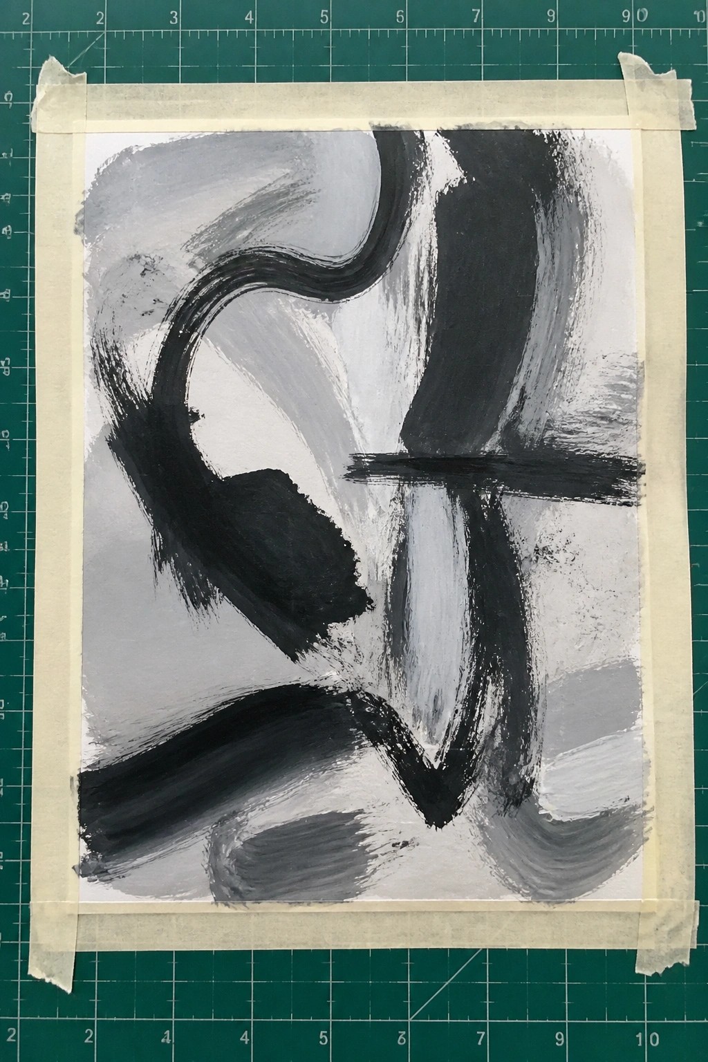 Abstract black and gray brushstrokes on white paper taped to green grid mat
