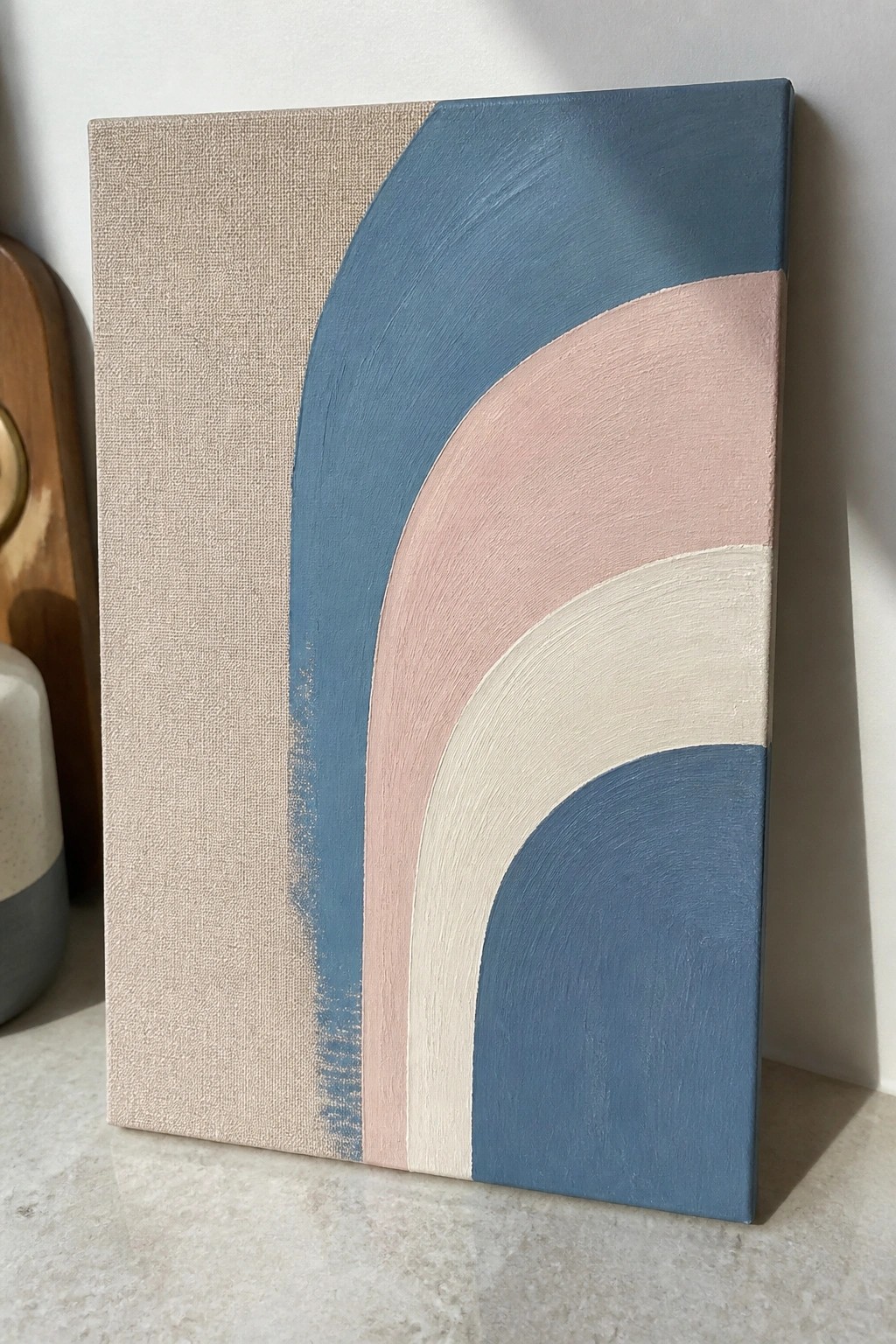Abstract painting with beige left panel and curved blue, pink, white bands on canvas.