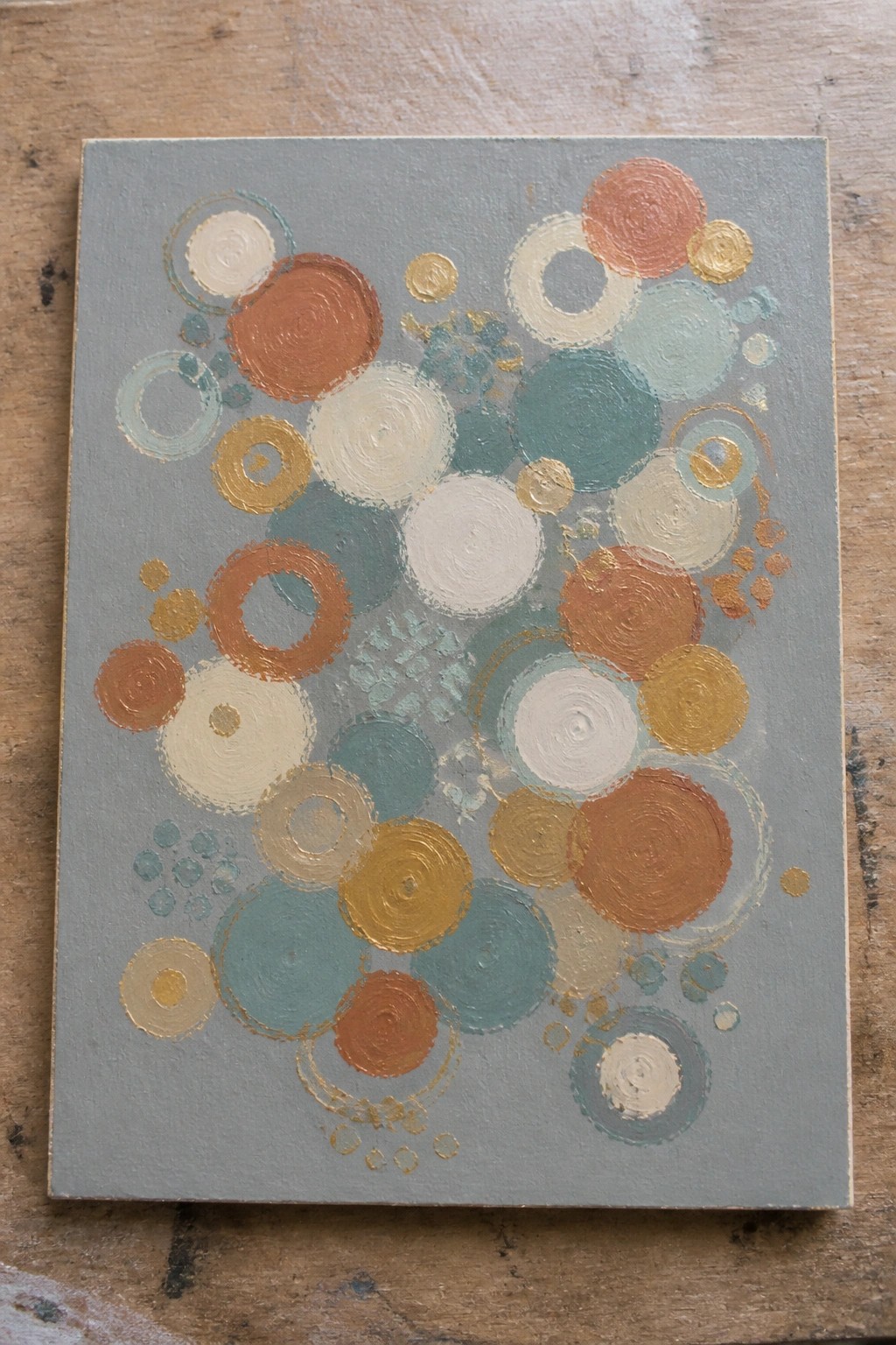 Abstract painting of overlapping circles in orange, teal, white and gold on gray canvas