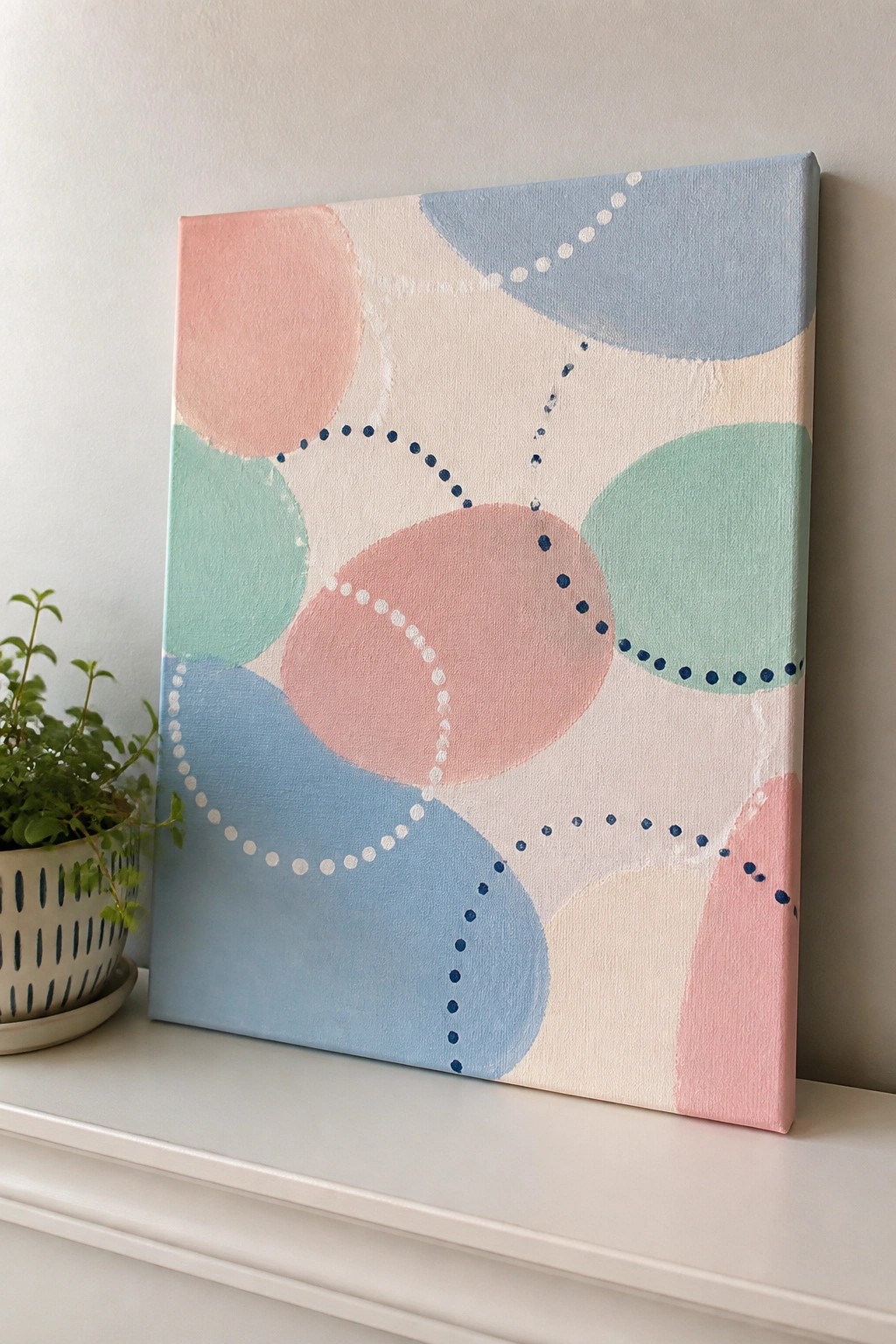 Pastel abstract canvas with overlapping circles and dotted lines beside a potted plant