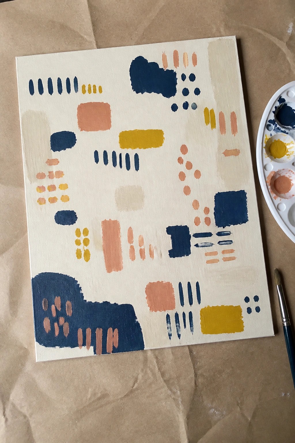 Abstract canvas with navy, peach, and yellow shapes beside palette and brush.